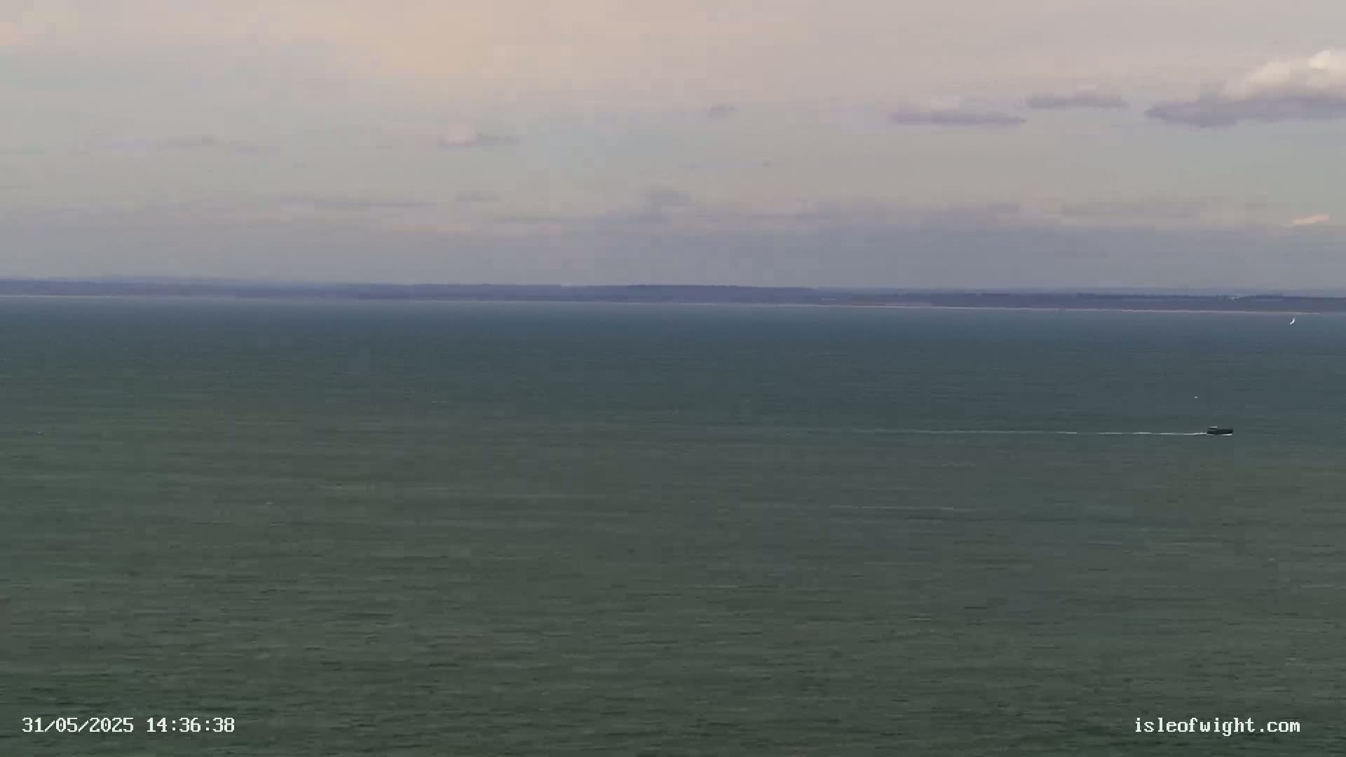 A wide shot of a calm, gray-green ocean under a mostly cloudy sky shows a small boat in the distance and a landmass on the horizon.