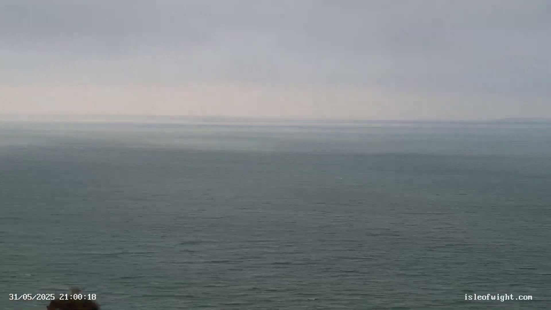 A calm, gray sea extends to a hazy horizon under an overcast sky.
