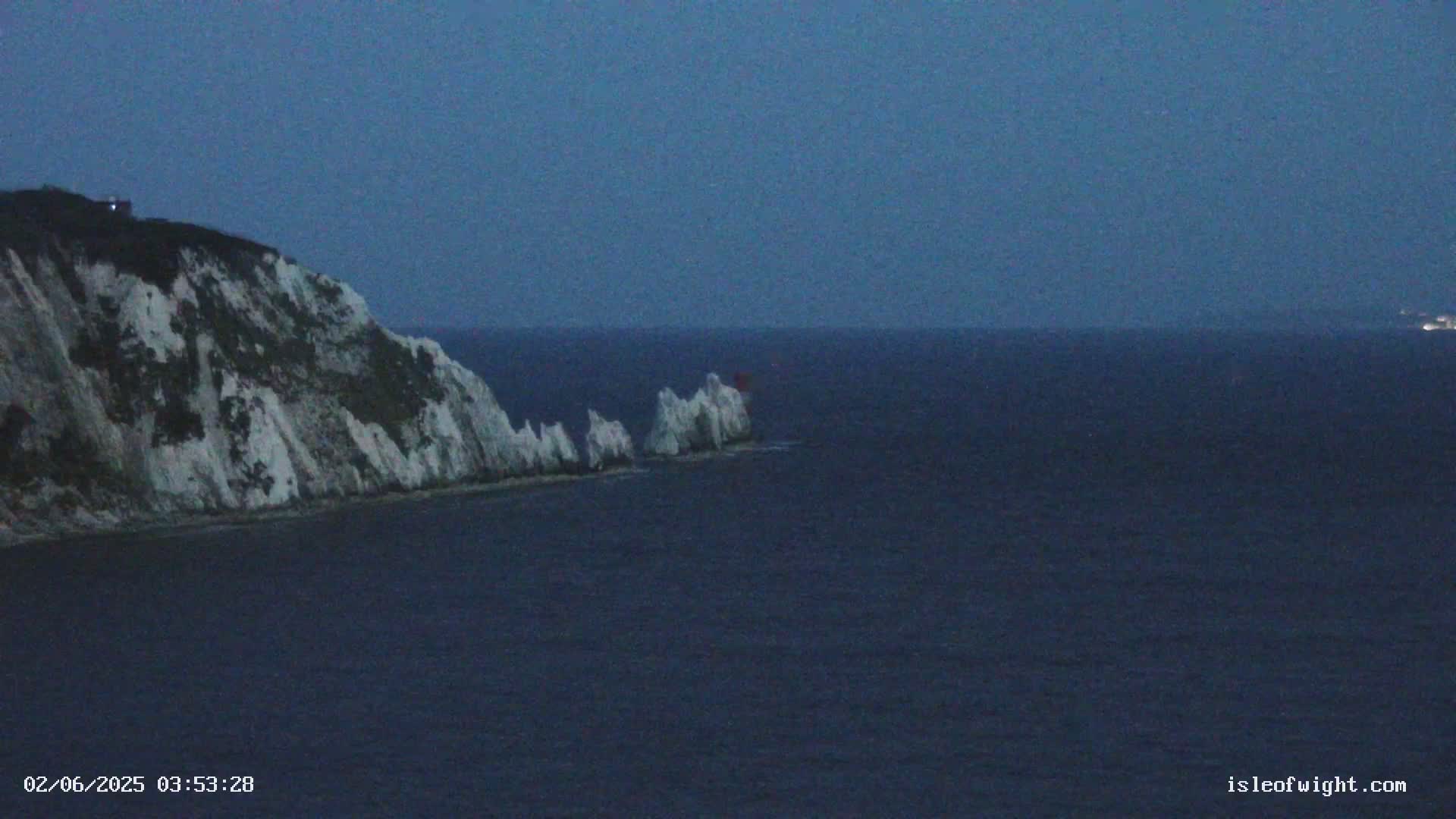 White cliffs rise from a dark blue sea under a twilight sky, with a smaller cluster of white rocks visible in the water.