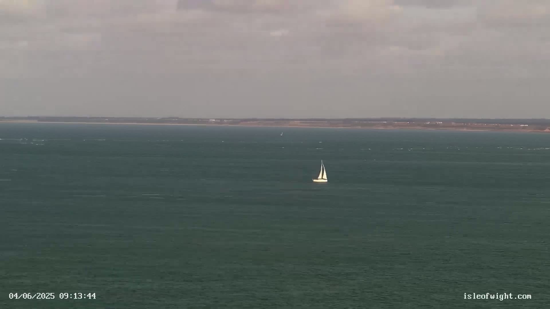A sailboat is visible on a dark-green sea under an overcast sky with a distant landmass in the background.