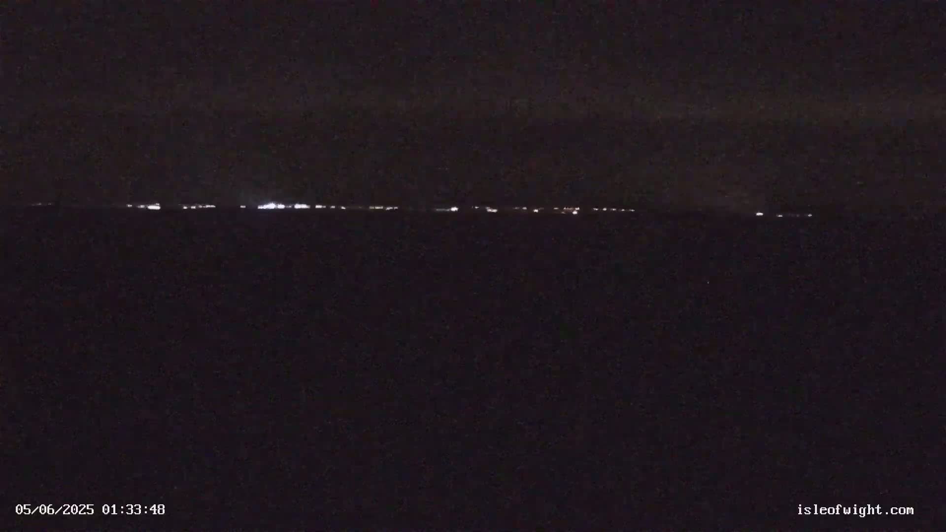 A dark, nighttime scene shows a faint line of distant lights on the horizon.