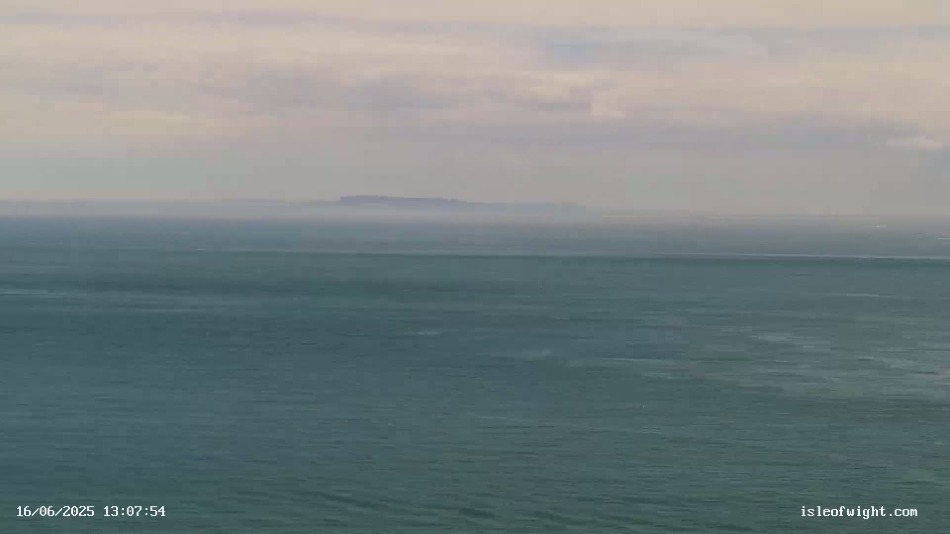 A hazy, overcast day reveals a distant island barely visible across a calm, dark teal sea.