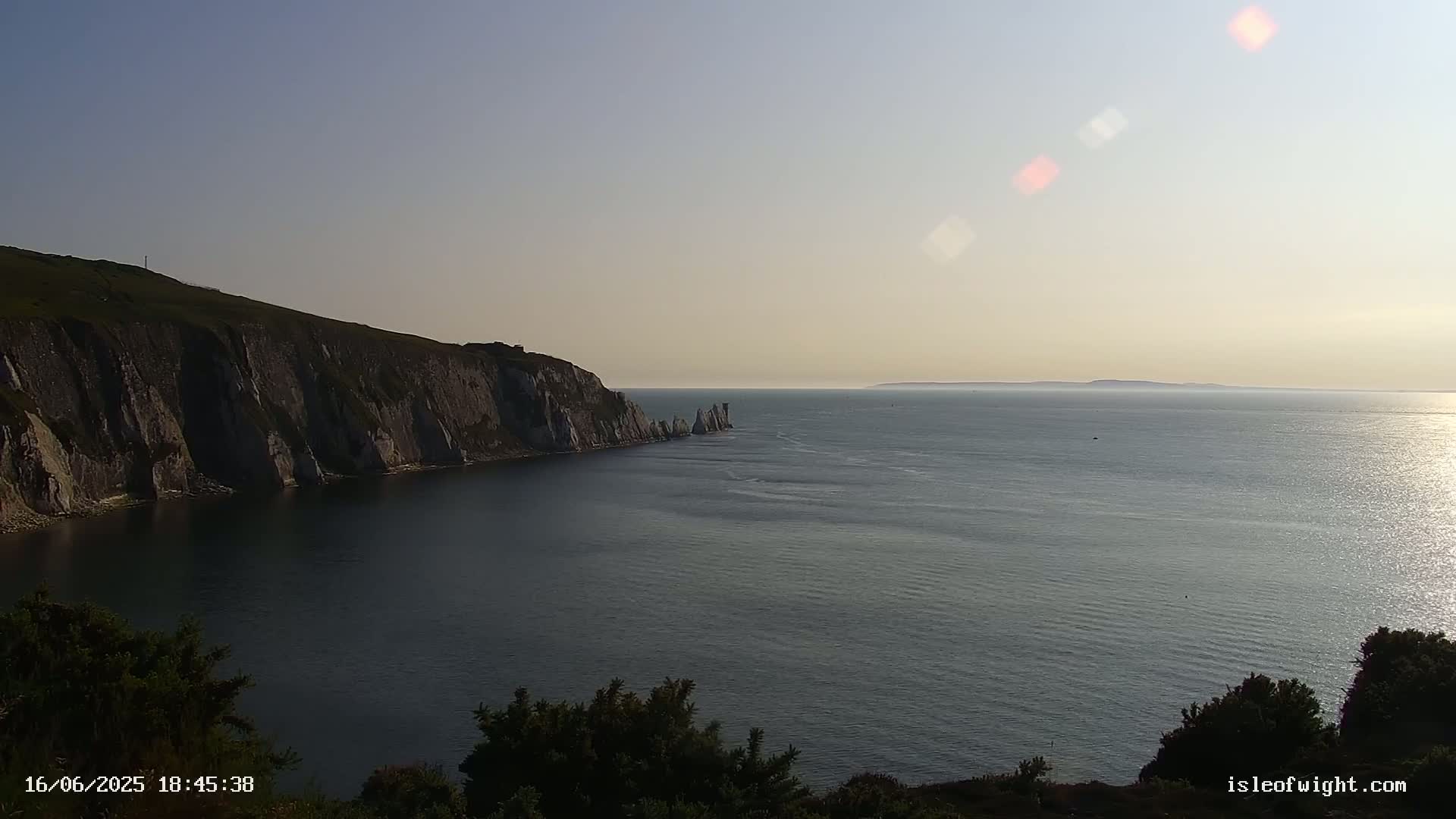 White cliffs meet a calm sea under a clear, bright sky, with a distant landmass visible on the horizon.