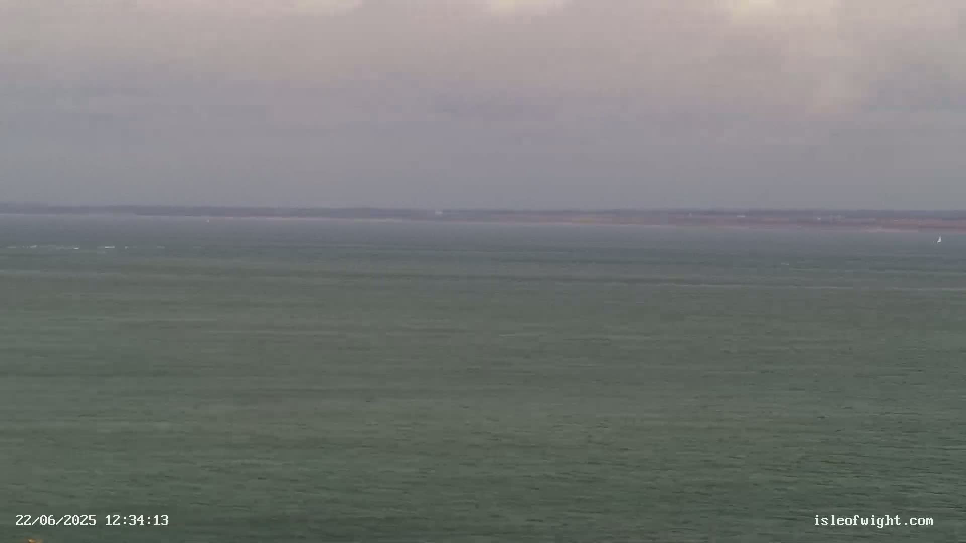 A calm, grey sea stretches to a distant, low-lying landmass under an overcast sky.