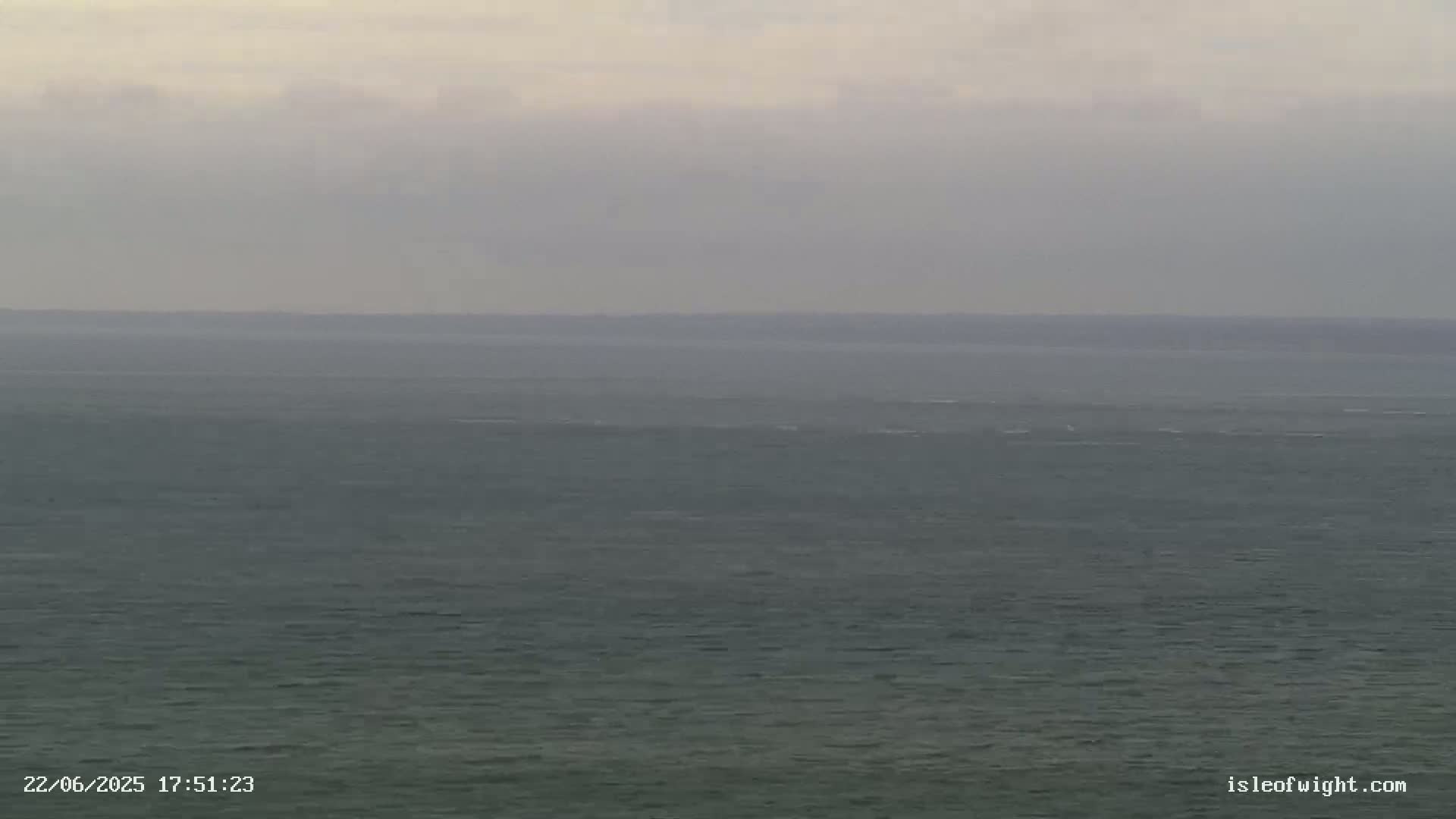 A calm, gray sea stretches to a hazy horizon under an overcast sky.