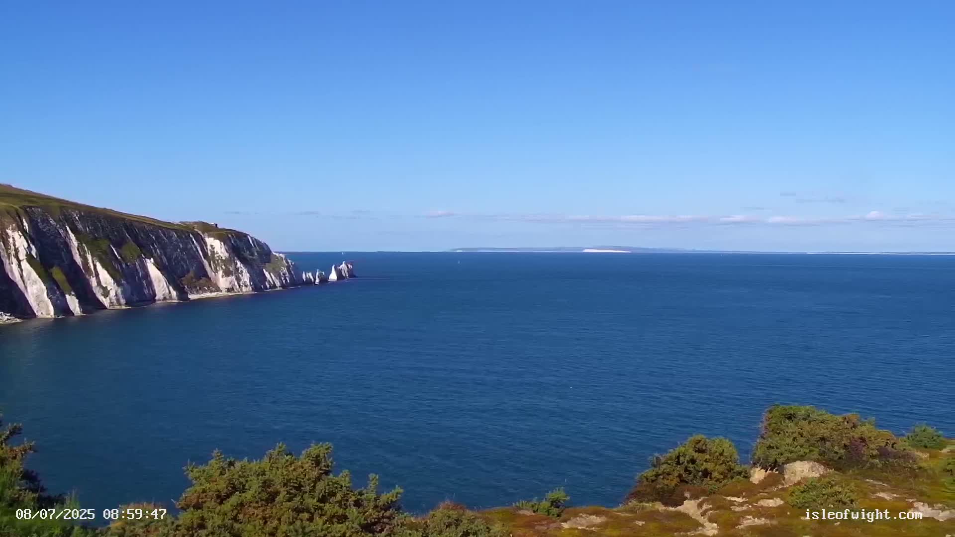White cliffs and rock formations extend into a calm, blue sea under a clear blue sky.