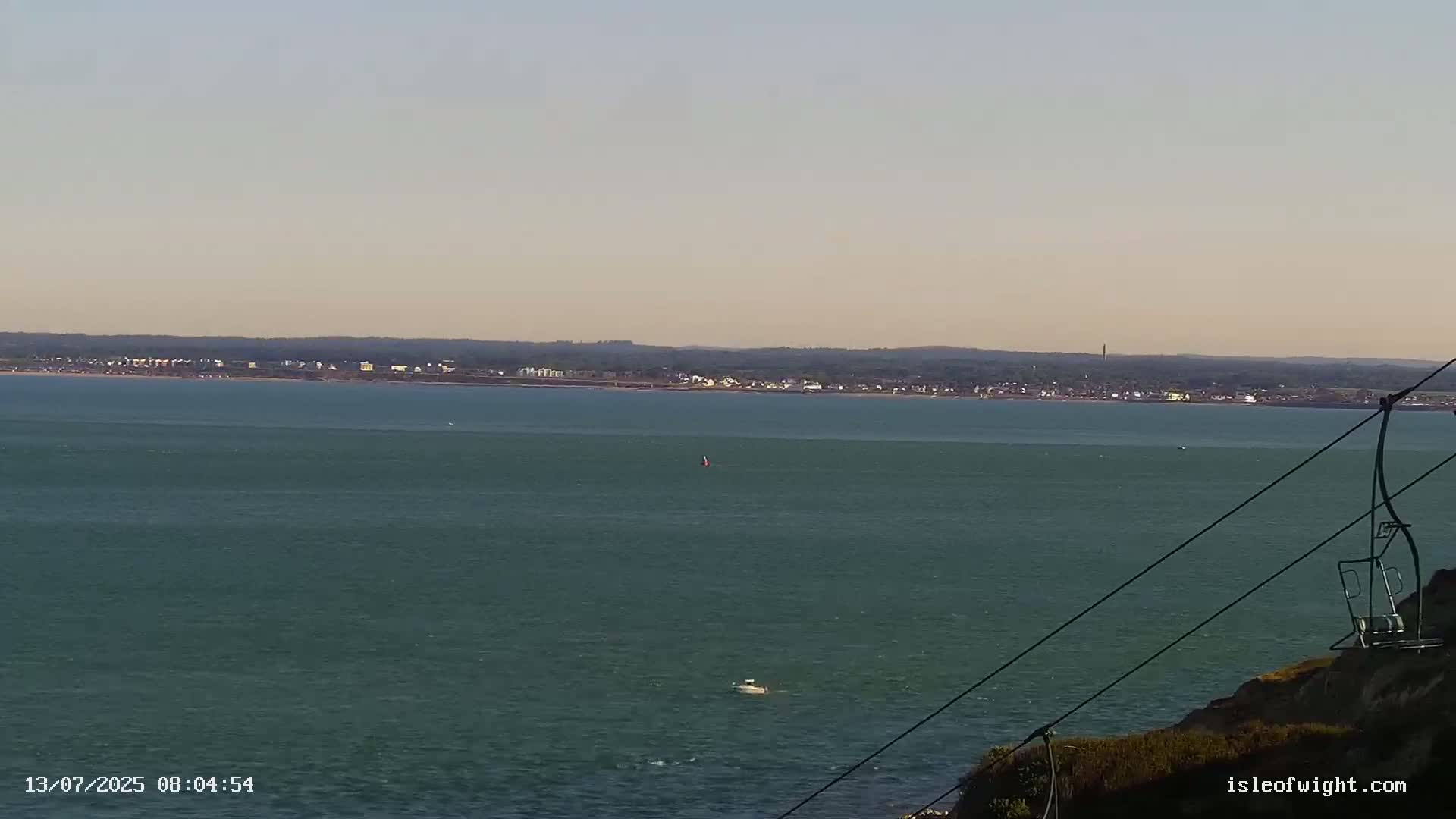 A calm, wide expanse of teal water stretches to a distant coastline under a clear sky, partially obstructed in the foreground by a chairlift.