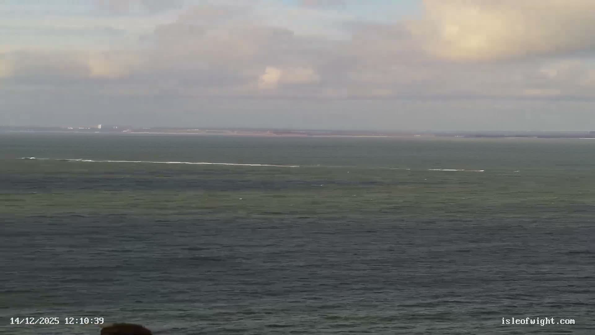 A red and white striped lighthouse stands amidst a series of rugged chalk stacks in rough, dark green-blue ocean waters with crashing waves under an overcast, stormy sky.