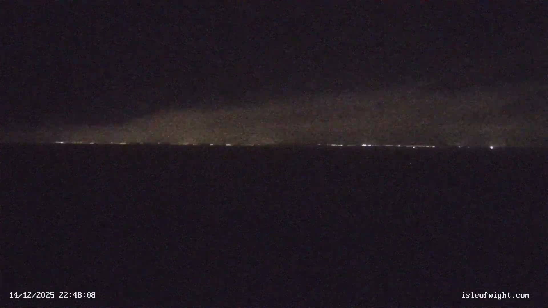 A red and white striped lighthouse stands amidst a series of rugged chalk stacks in rough, dark green-blue ocean waters with crashing waves under an overcast, stormy sky.