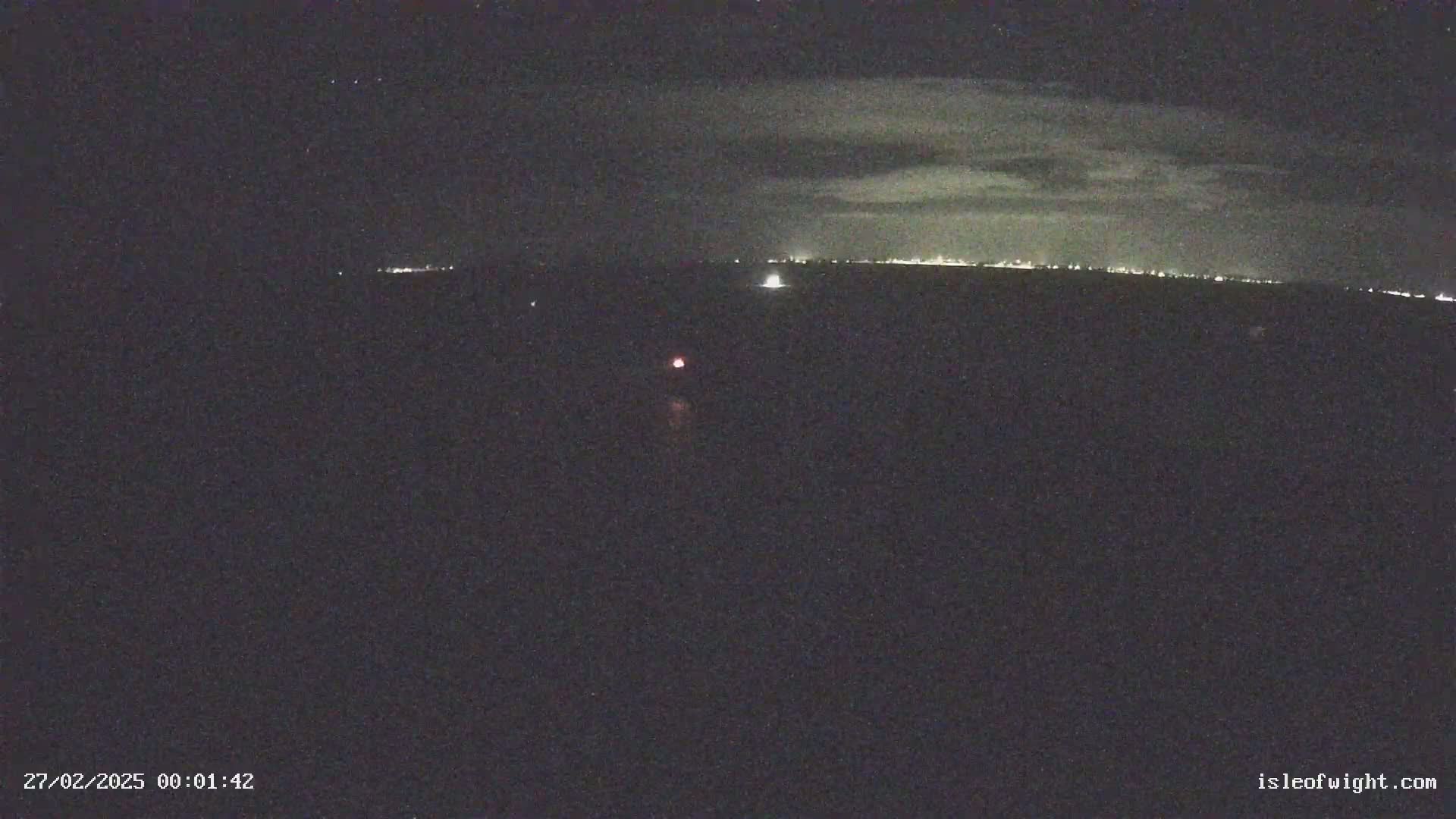 A nighttime, long-range view shows a distant city skyline illuminated against a dark sky with faint clouds.