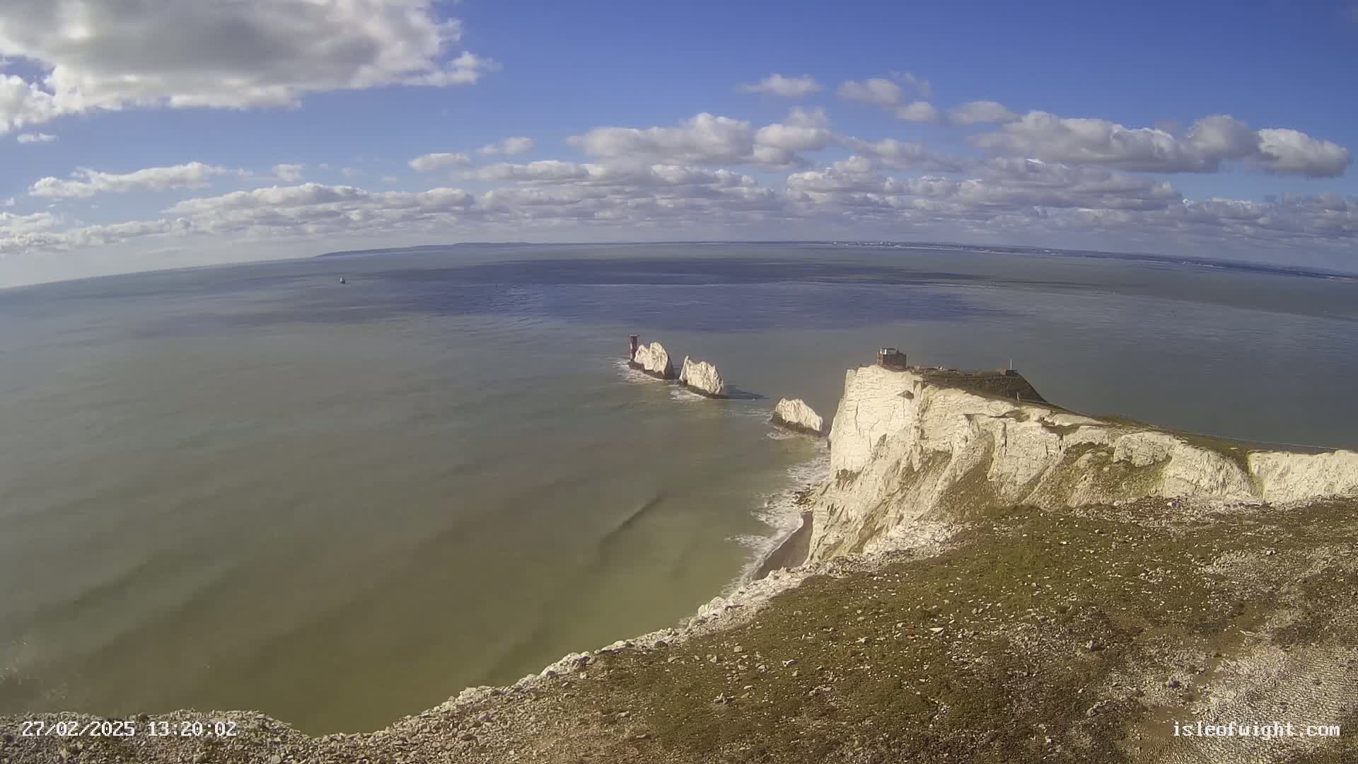 White cliffs overlook a calm sea where several rock formations rise from the water under a partly cloudy sky.