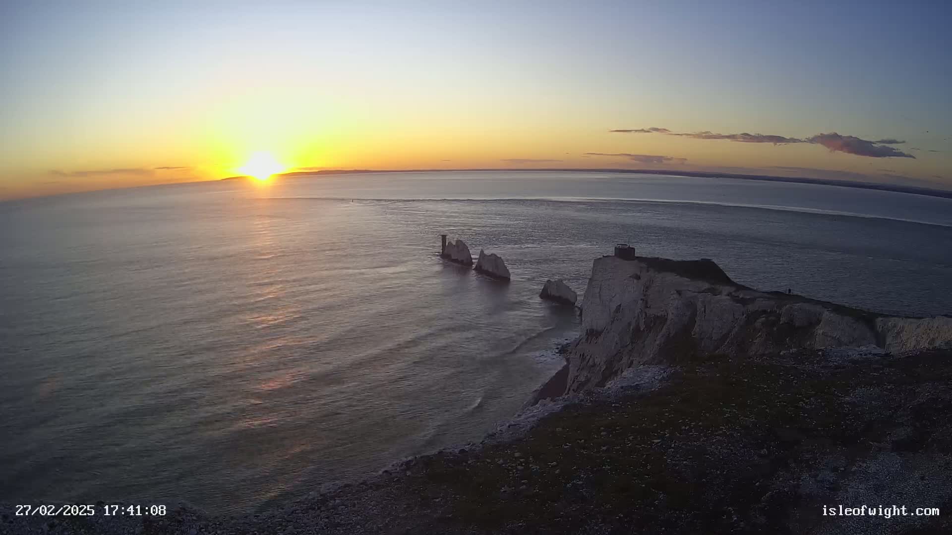 A sunset over a calm ocean shows white cliffs with several rock formations jutting out into the water.