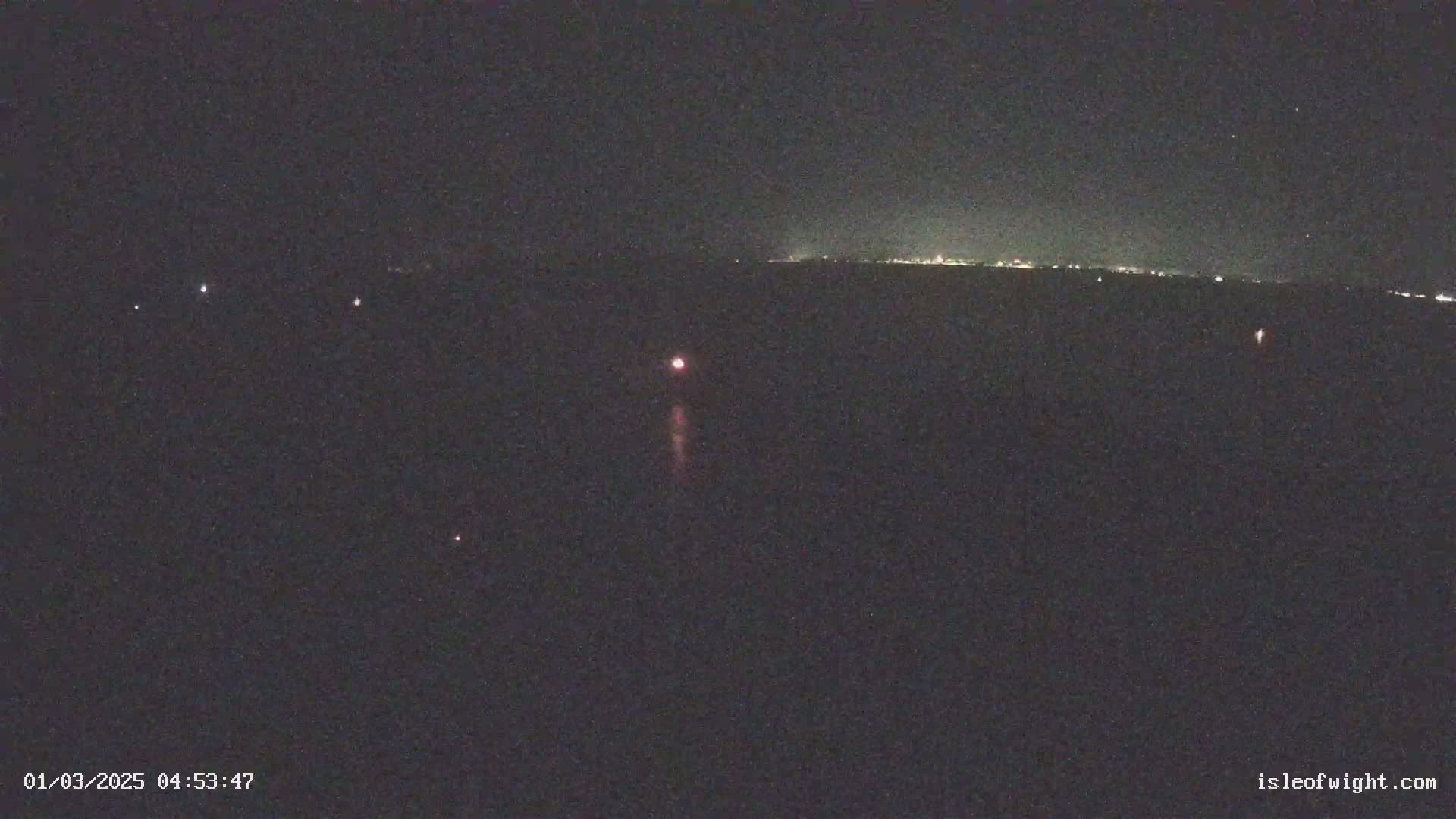 A nighttime long shot shows a dark landscape with a few faint lights in the distance and a bright light with a trail in the center, possibly a distant town or city lights and a flare.