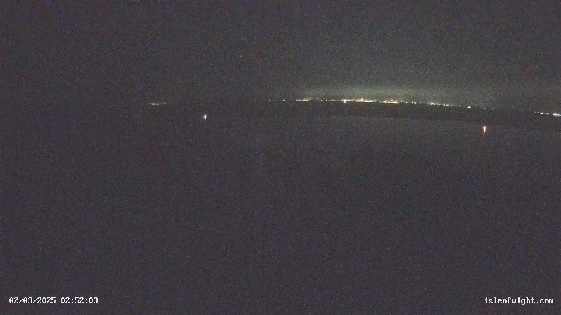 A nighttime long shot shows a dark, flat expanse of land with a distant line of lights on the horizon under a clear, dark sky.