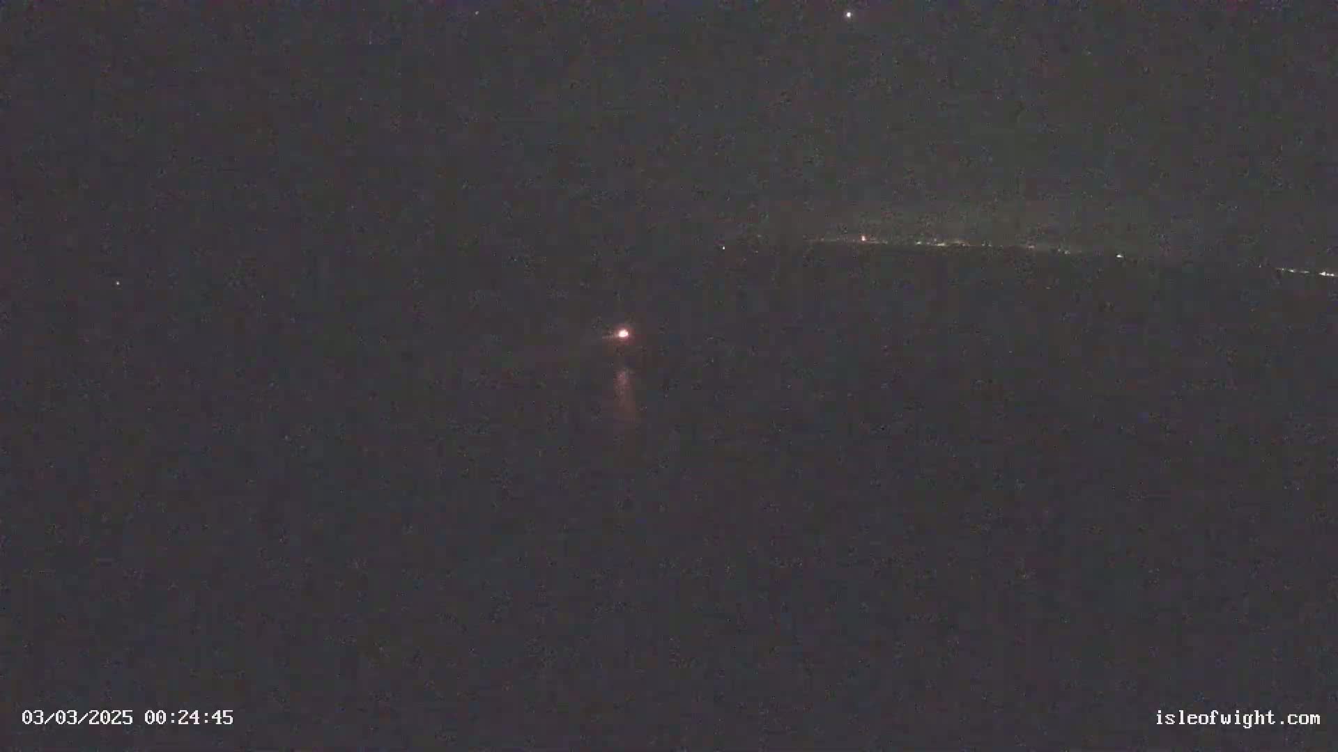 A nighttime long-range view shows a faint, reddish light in the distance, possibly a distant light source or atmospheric phenomenon, under a clear, starry sky.