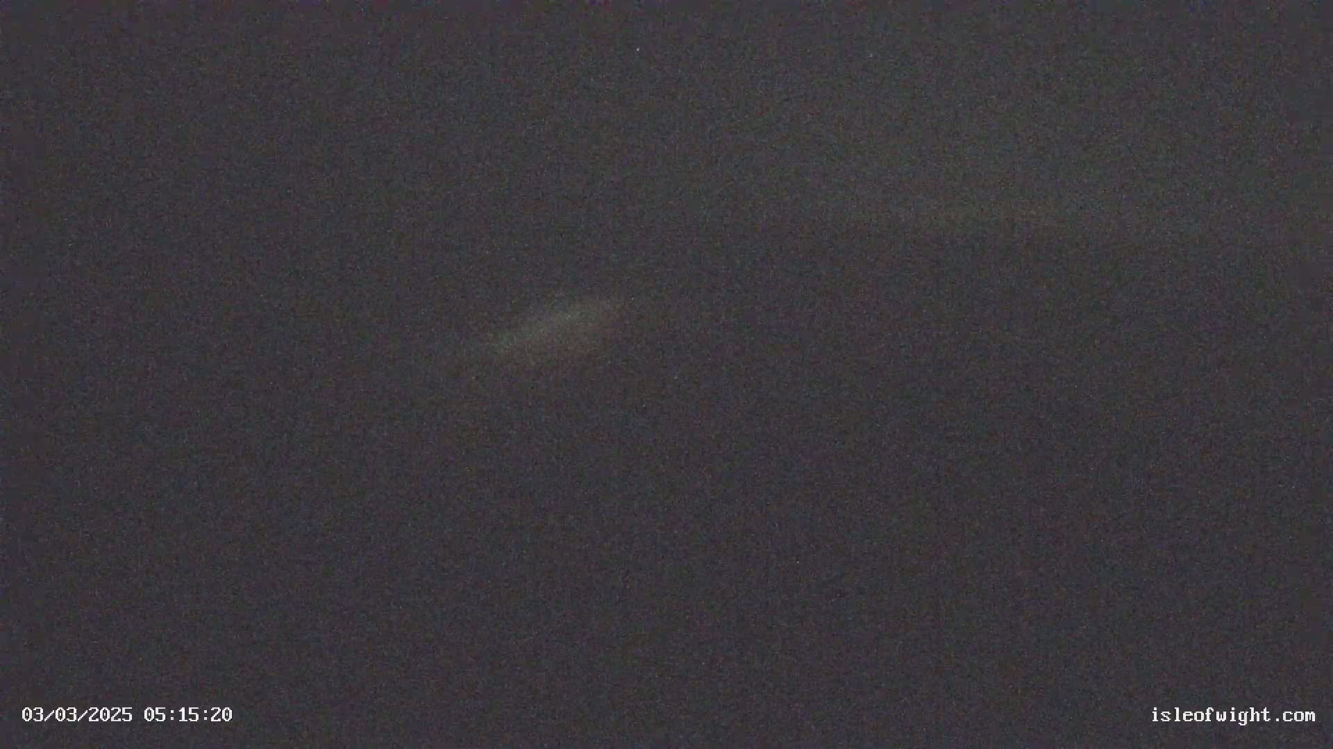 A dark, nighttime scene shows a faintly lit area in the center, possibly indicating a light source or atmospheric phenomenon.