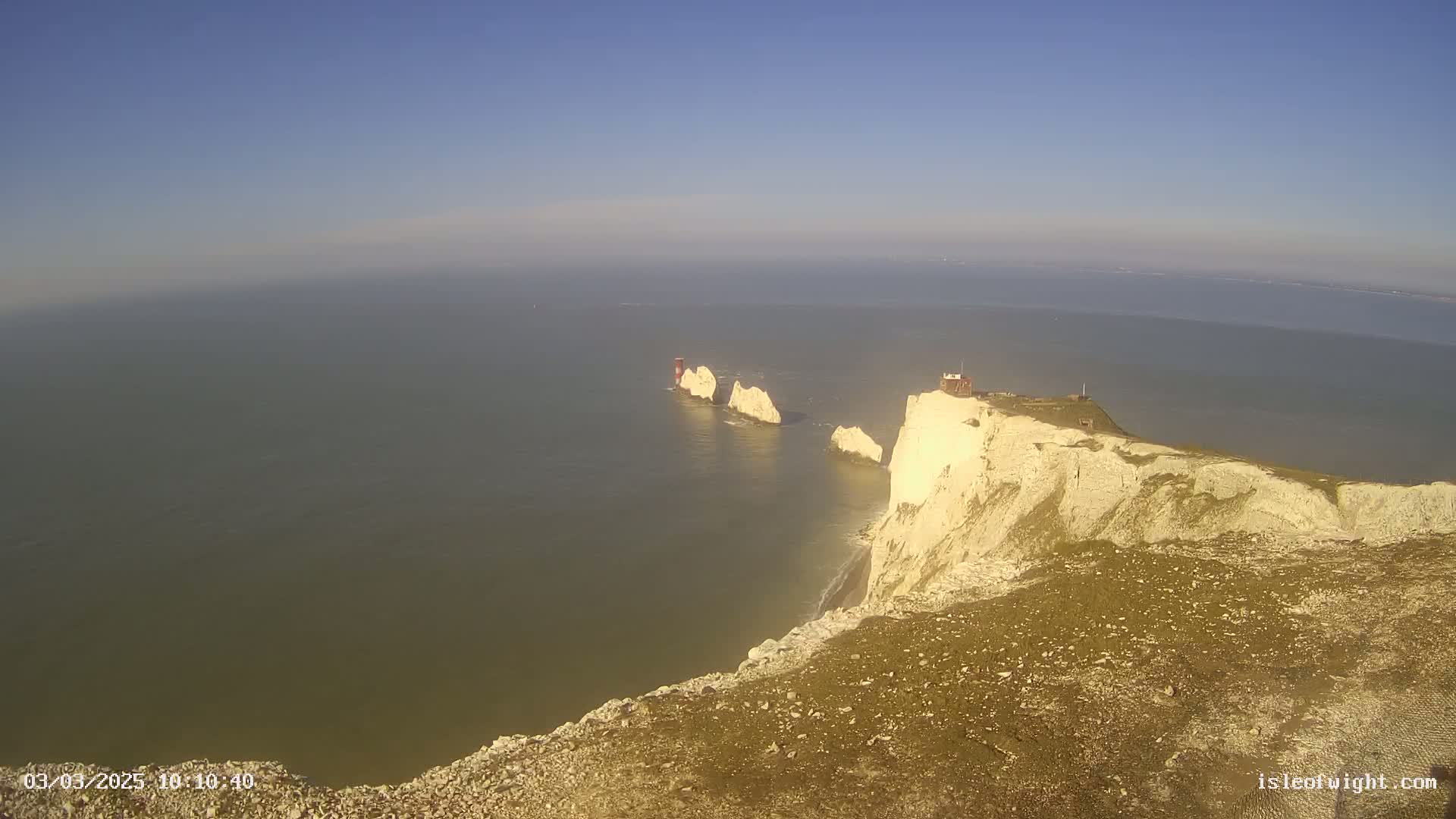 High-angle view of white cliffs meeting a calm sea with a group of smaller white rock formations in the water.