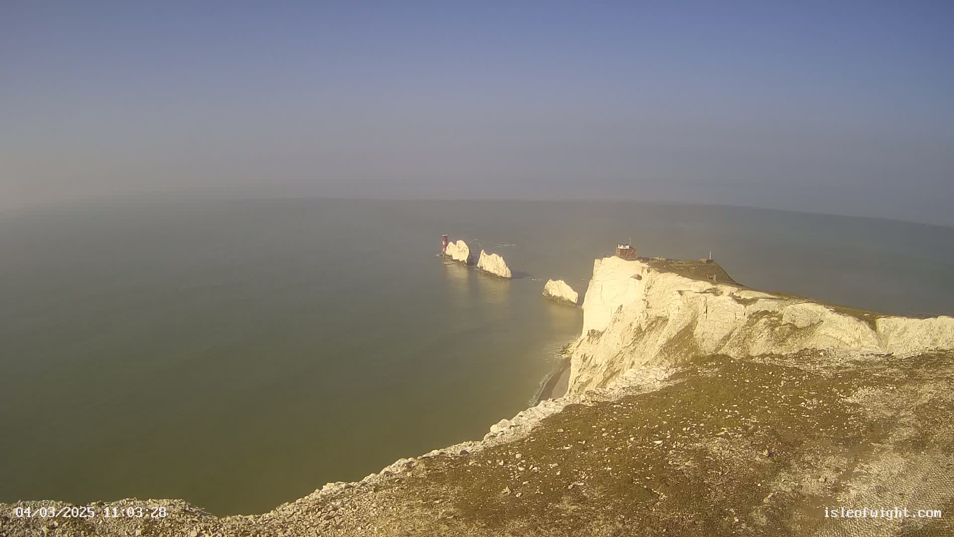 White cliffs overlooking a hazy sea with several smaller white rock formations extending from the cliffs into the water.