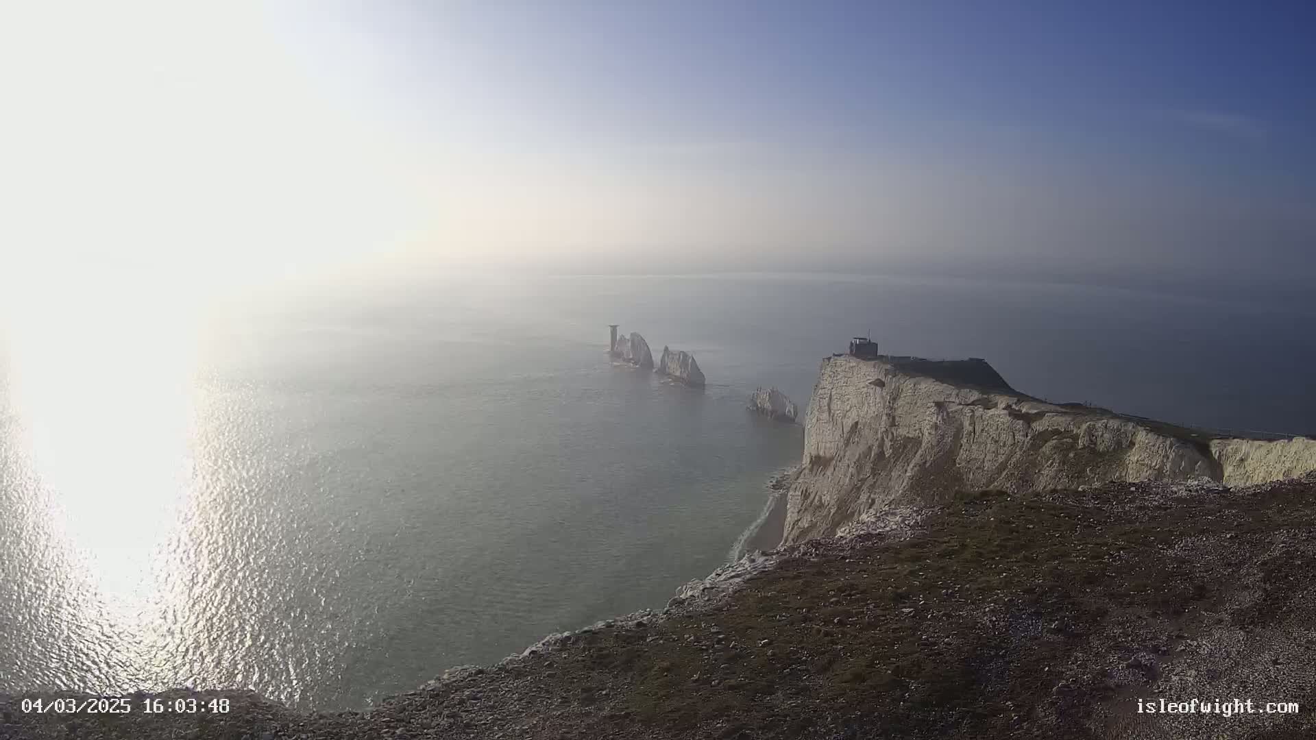 White cliffs overlook a hazy sea with several small, distant white rock formations.