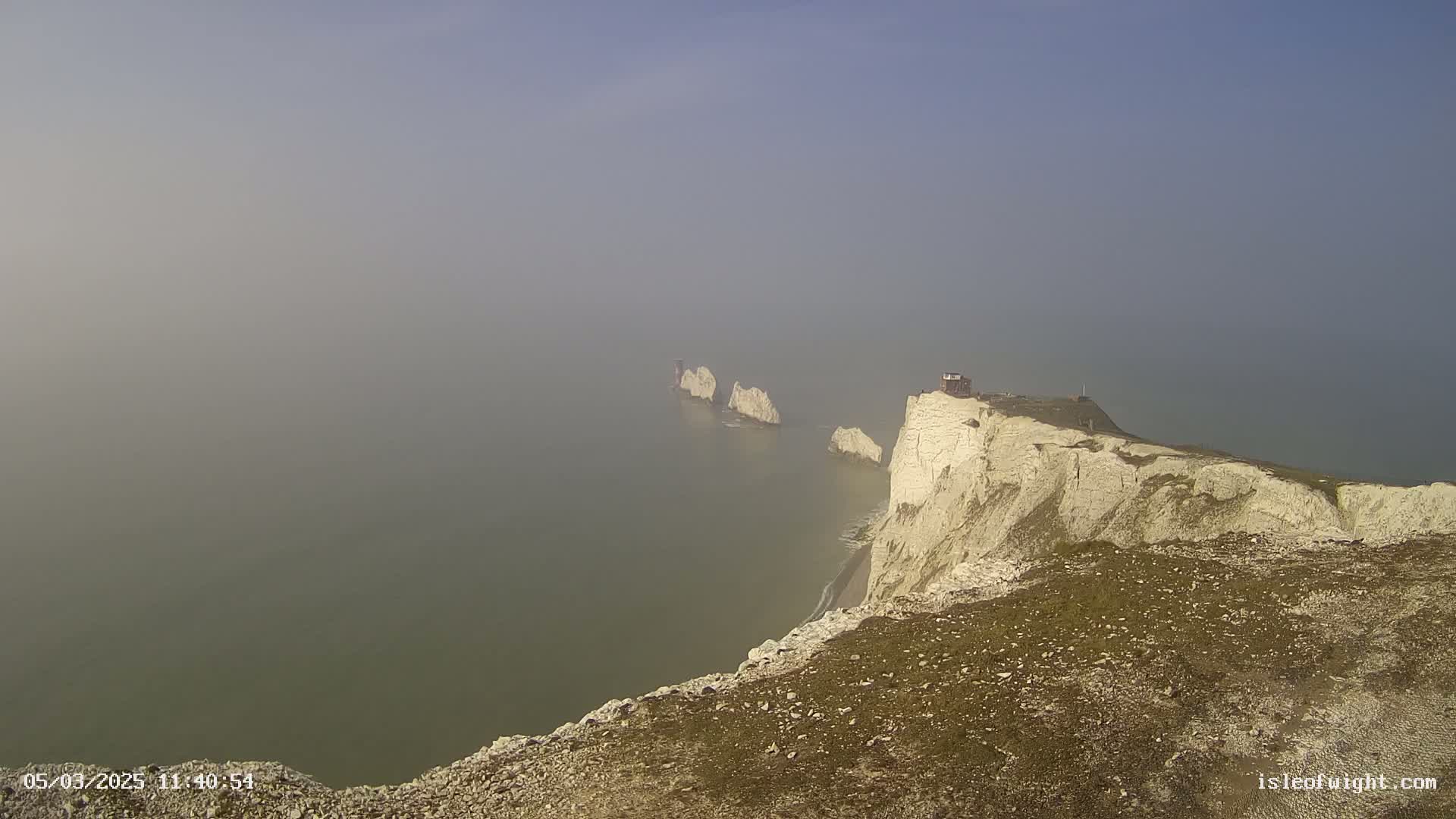 White cliffs overlook a foggy sea with several stacks visible in the distance.