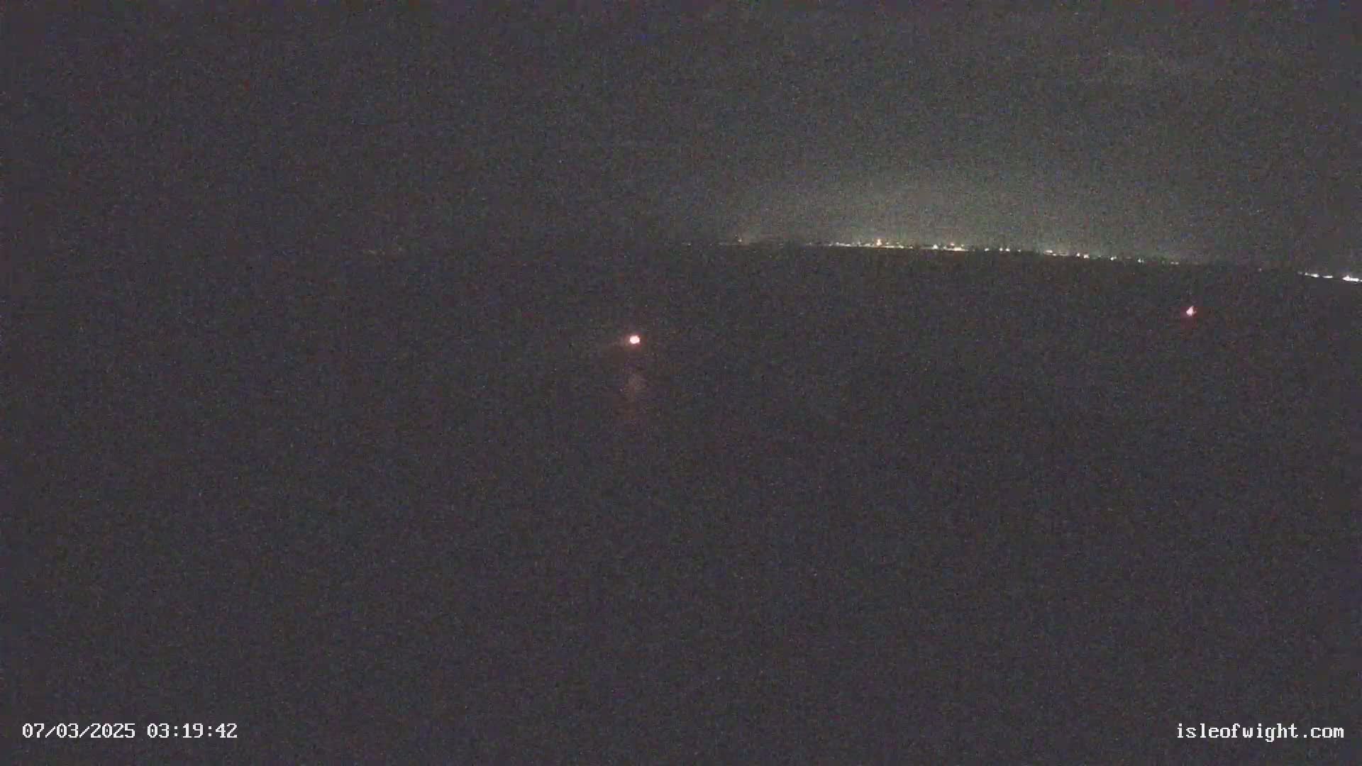 A dark, nighttime scene shows a distant, faintly lit horizon and two small, reddish lights in the foreground.