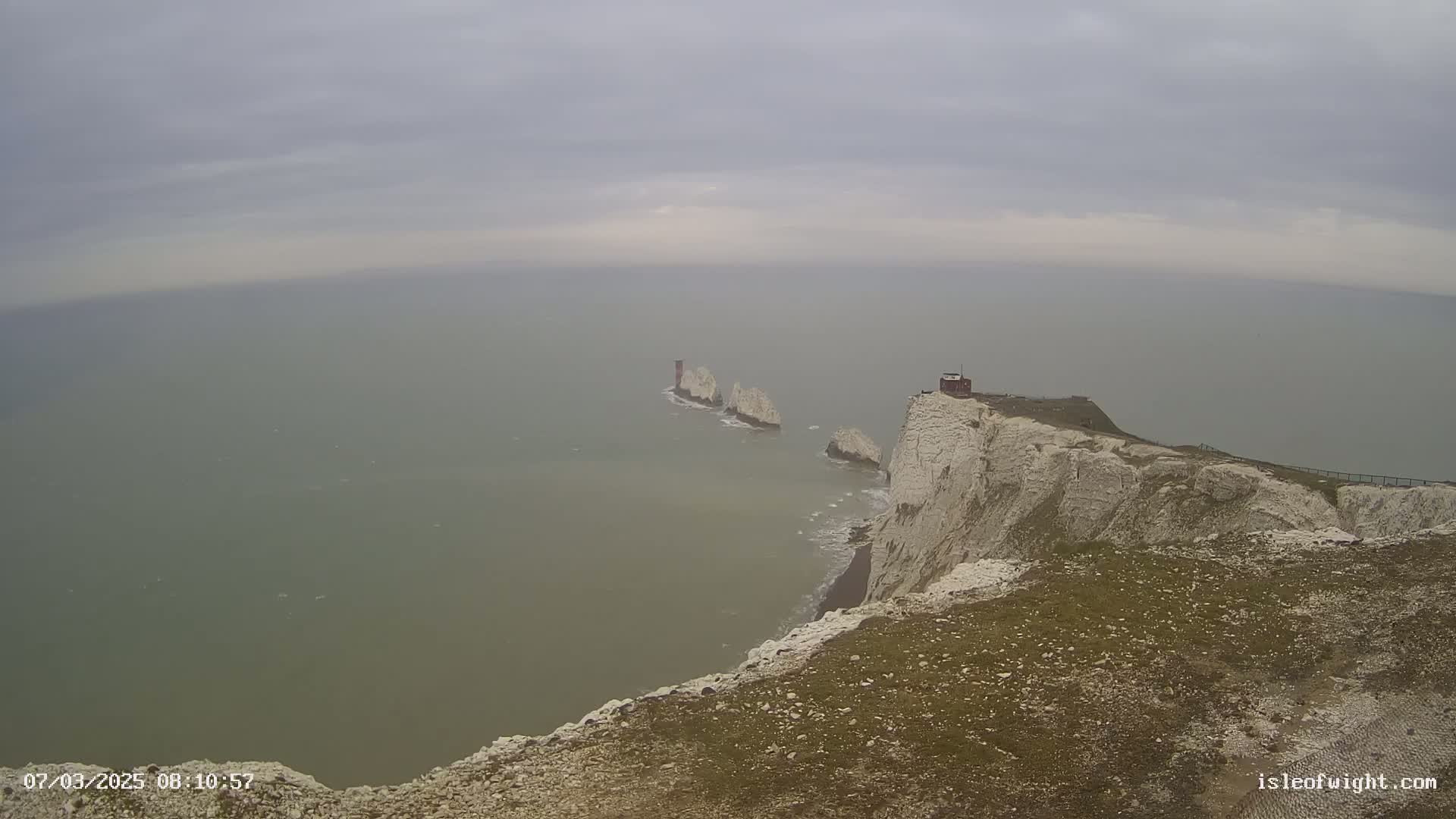 A high vantage point overlooks a foggy sea with white cliffs and several stacks visible in the distance.