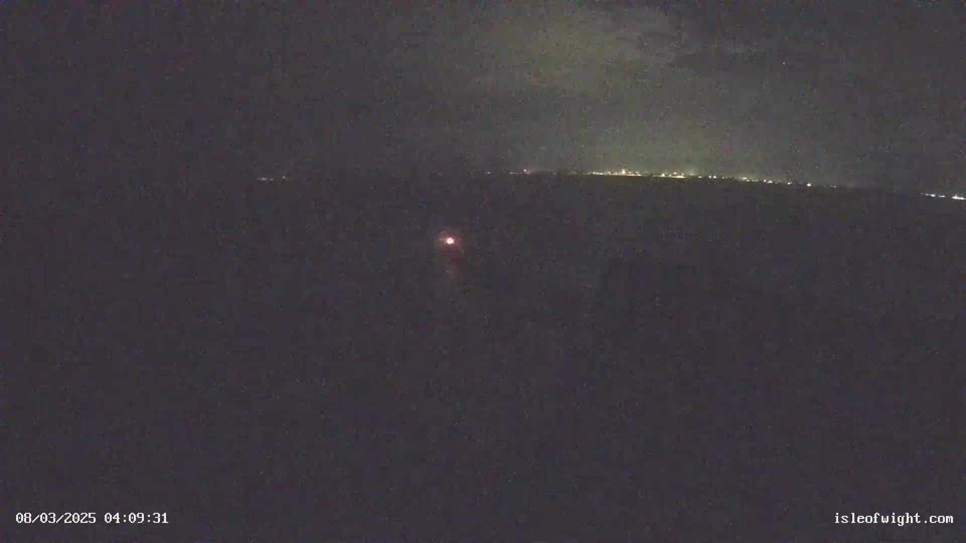 A dark, nighttime scene shows a distant line of lights on the horizon and a single, small light closer to the camera.