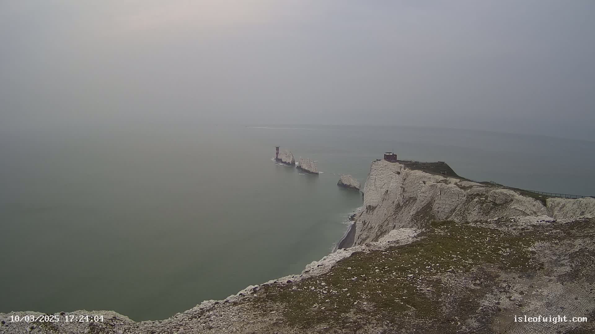 White cliffs overlook a hazy sea and a line of rocky islands extending from the cliff.