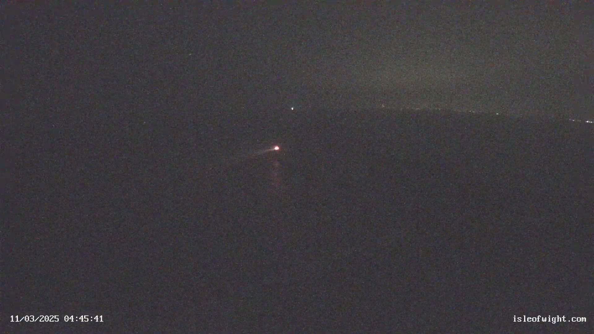 A dark, nighttime scene shows a faint, reddish light low on the horizon and a fainter light higher in the sky, with a dark landmass visible on the horizon.