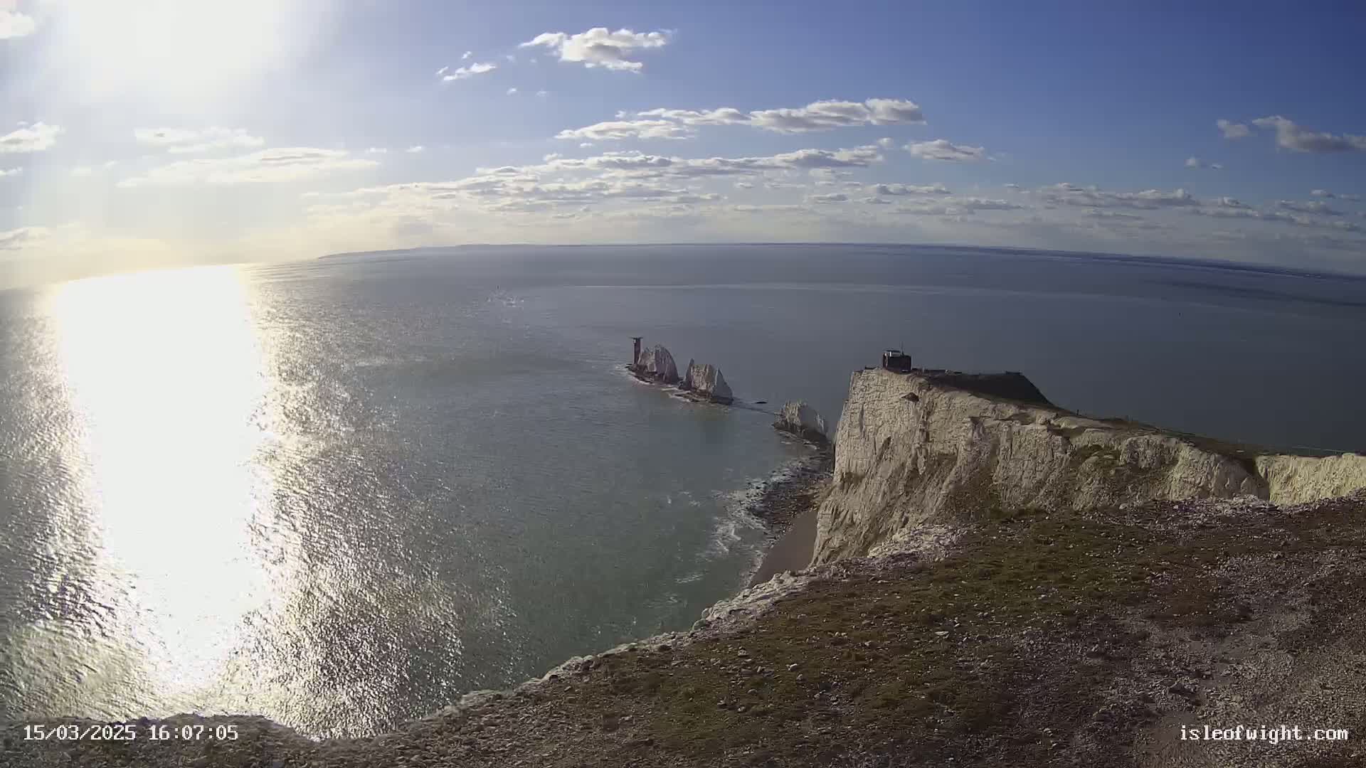 A sunny day shows white cliffs overlooking a body of water where a small island with a lighthouse is visible in the distance.