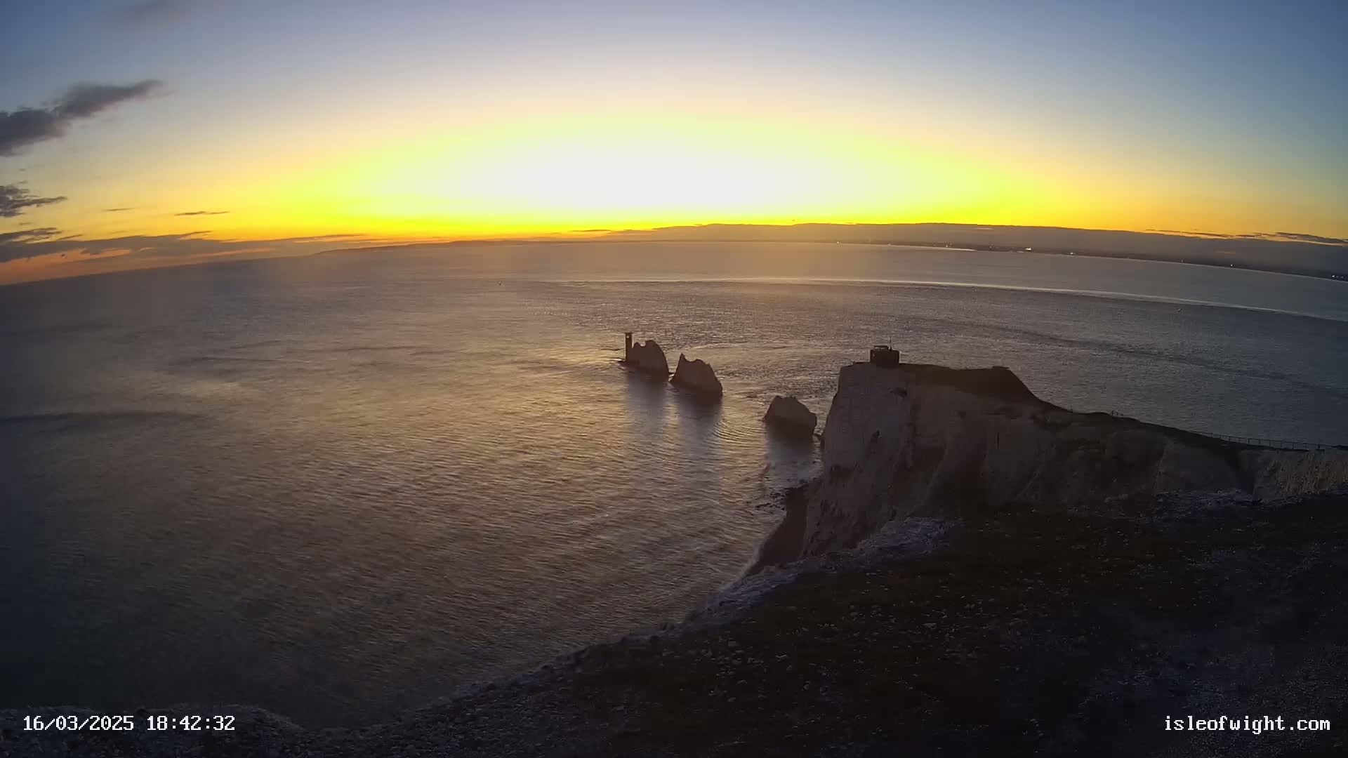 A sunset over a calm ocean with several prominent rock formations visible from a cliffside vantage point.
