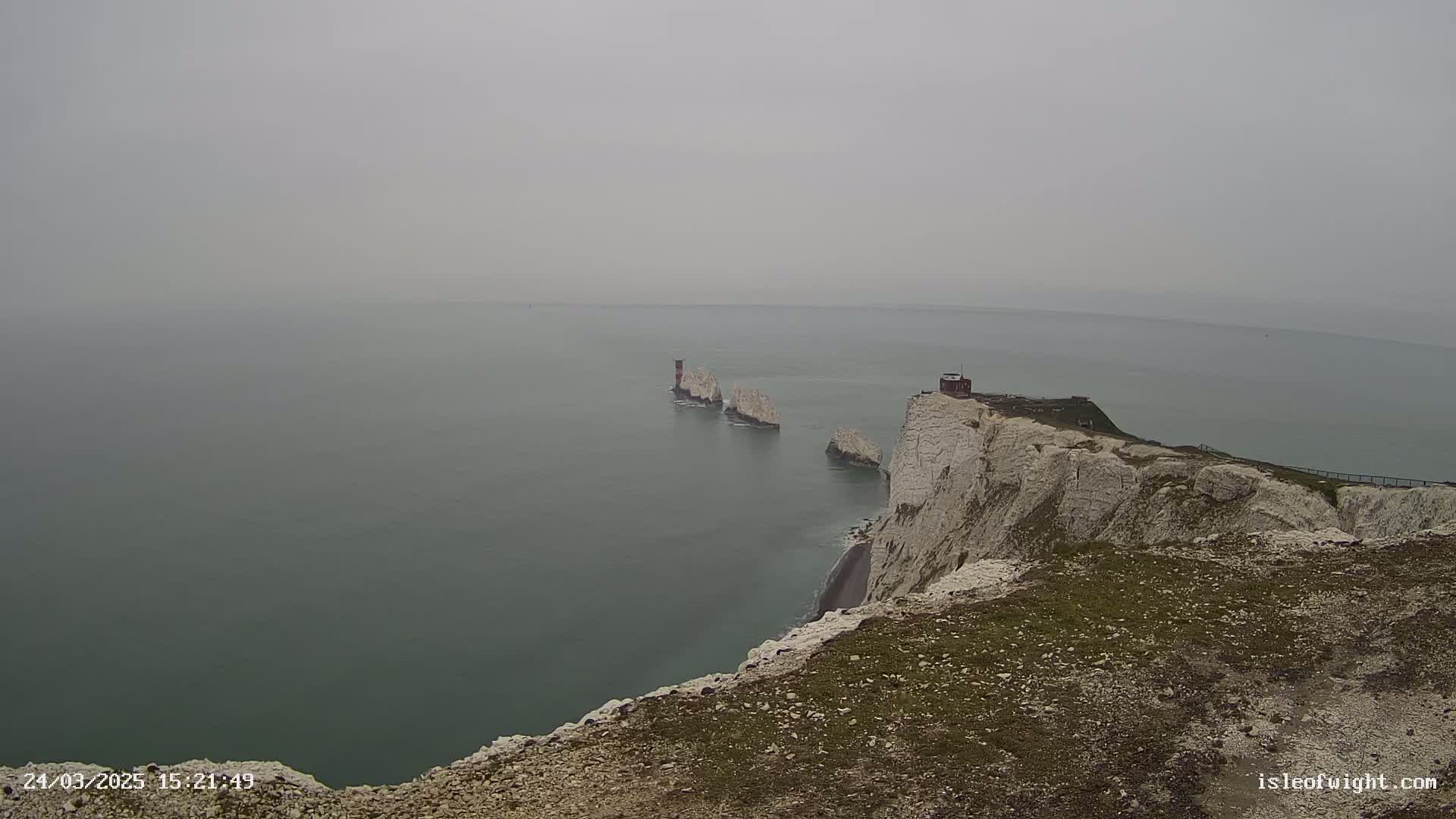 A hazy view shows a line of white cliffs and stacks extending into a calm, grey sea.