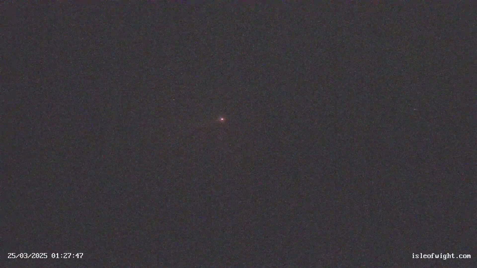 A single, faint, reddish light is visible in a dark, nighttime sky.