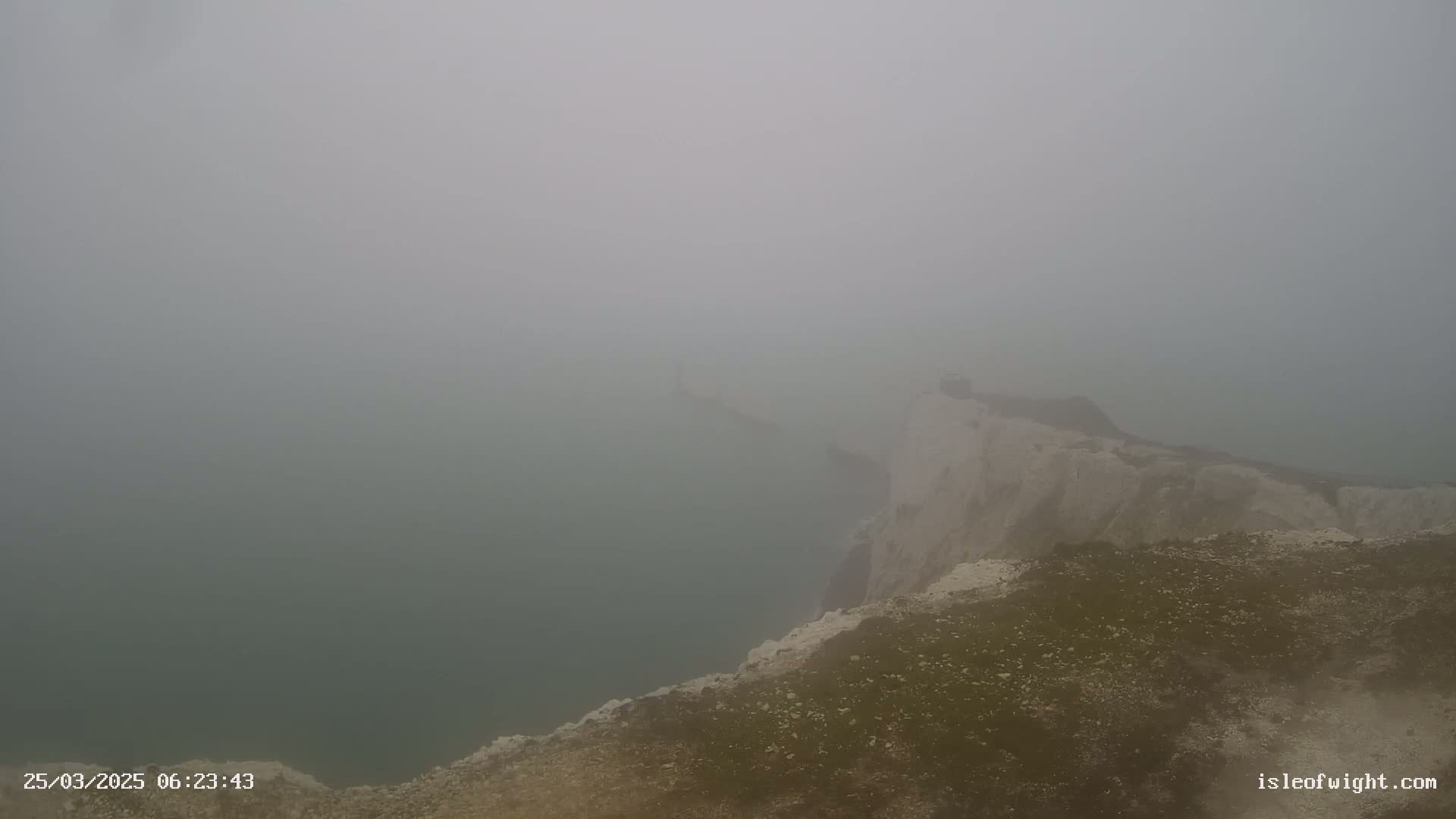 A foggy view from a cliff top overlooking a body of water.