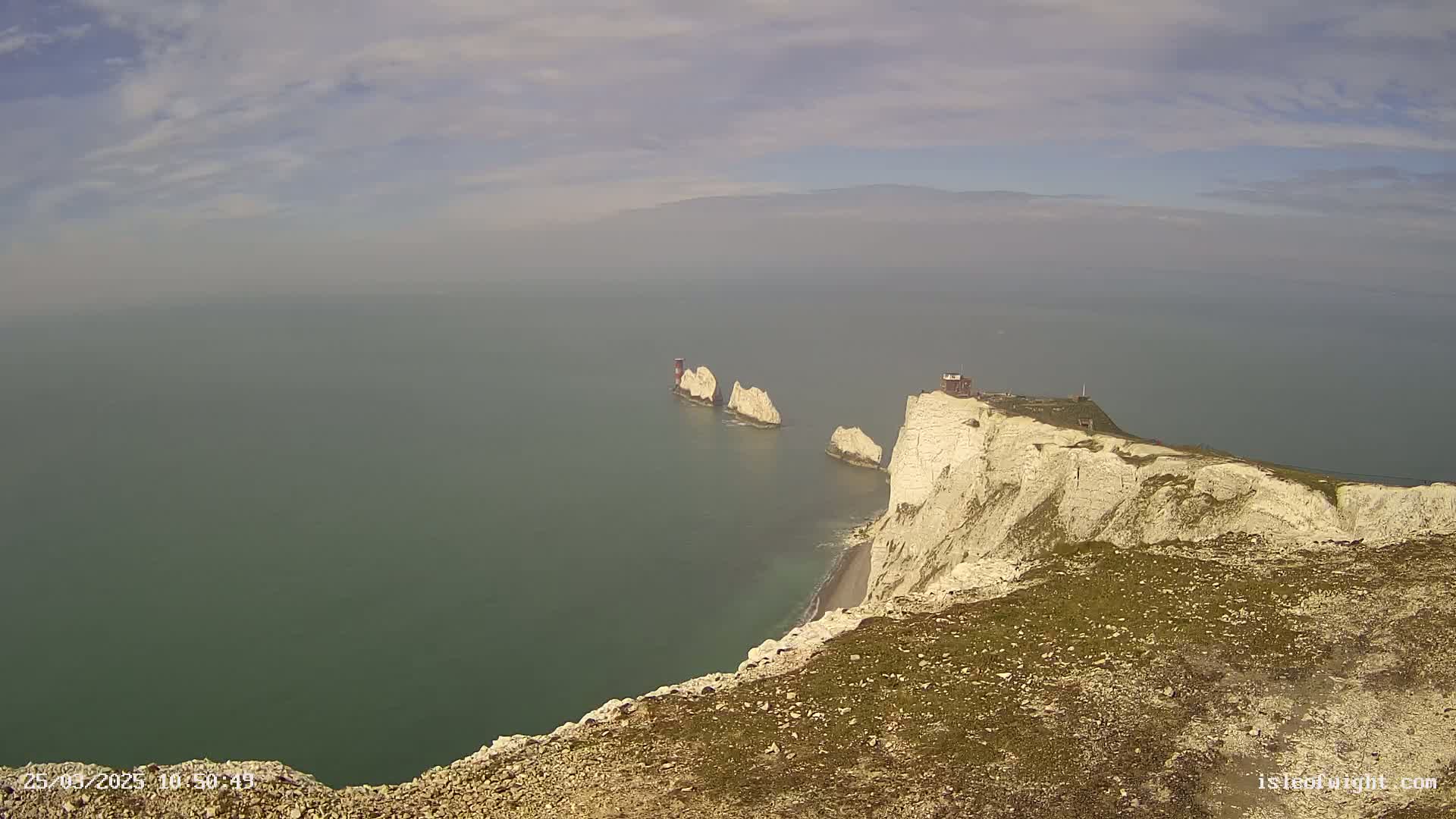 White cliffs overlooking a hazy, green ocean with three smaller rock formations offshore.