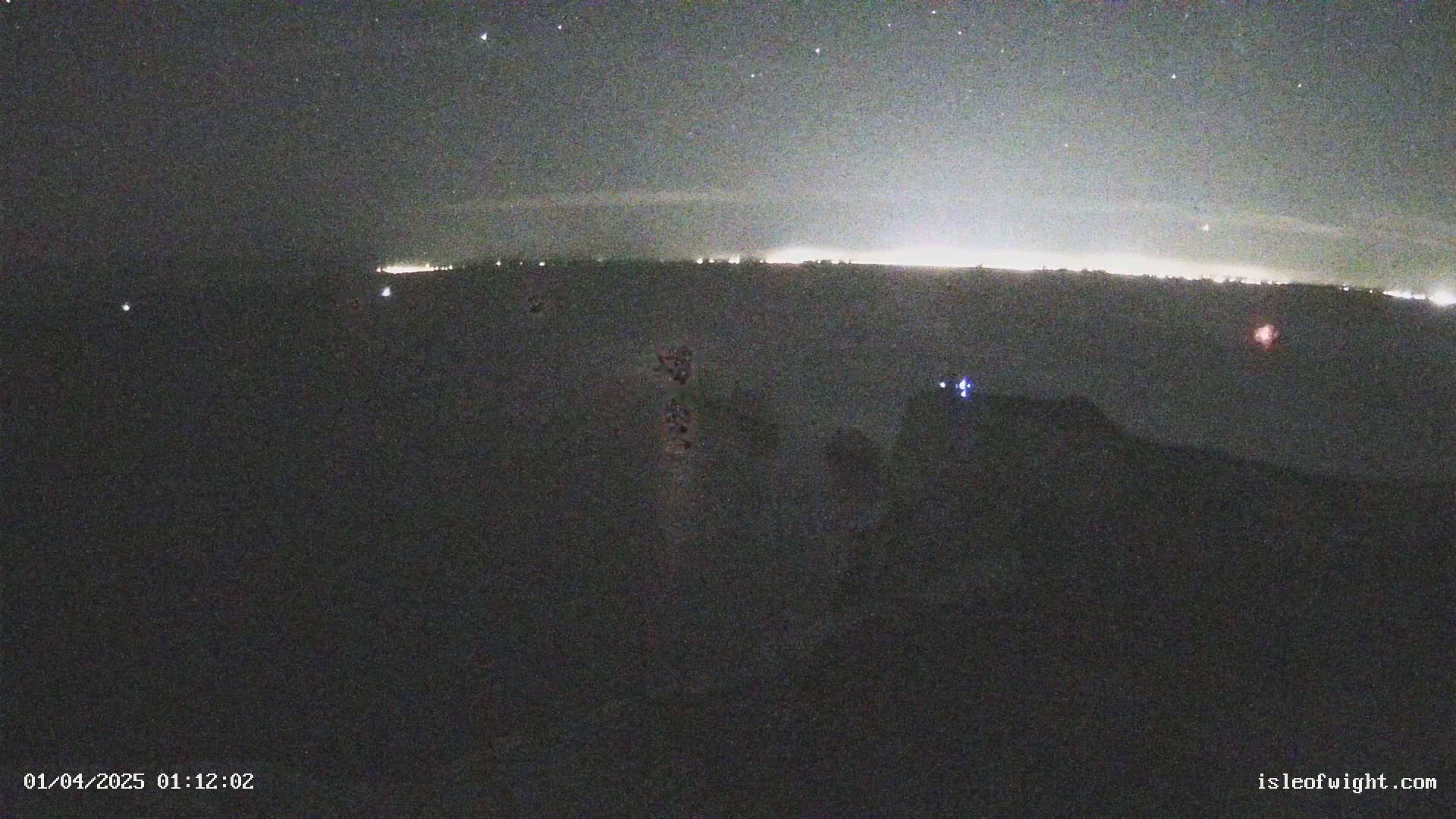 A nighttime long shot shows a distant horizon illuminated by faint lights under a starry sky.