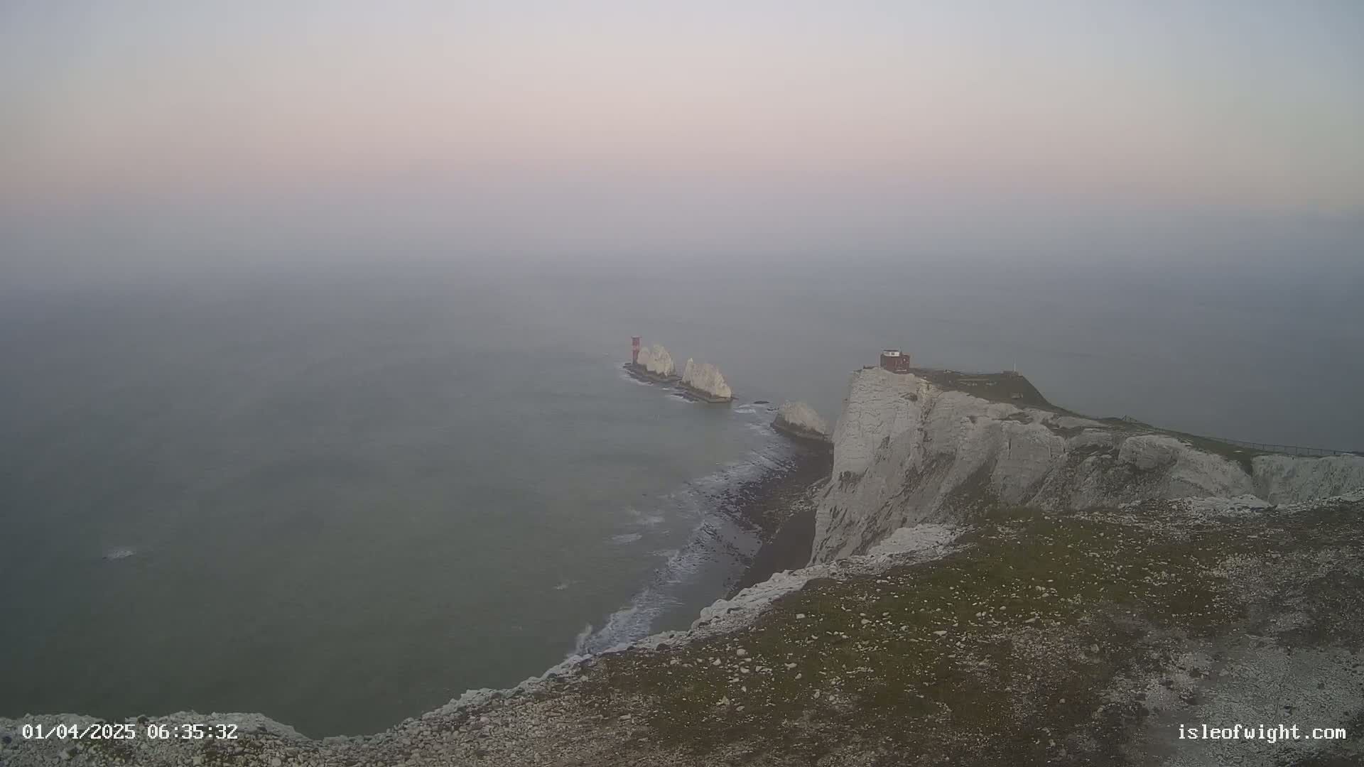 White cliffs meet a foggy sea where a small island with a lighthouse is visible in the distance.
