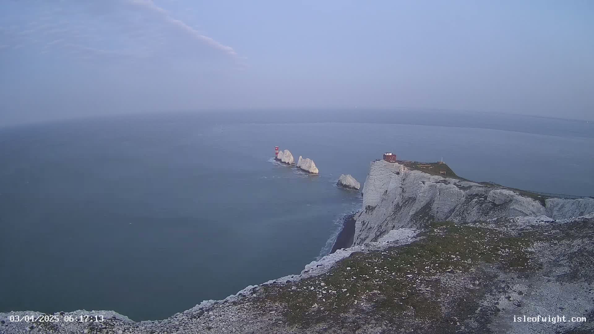 A hazy view of white cliffs overlooking the ocean, with a group of smaller white rock formations and a red structure visible in the distance.