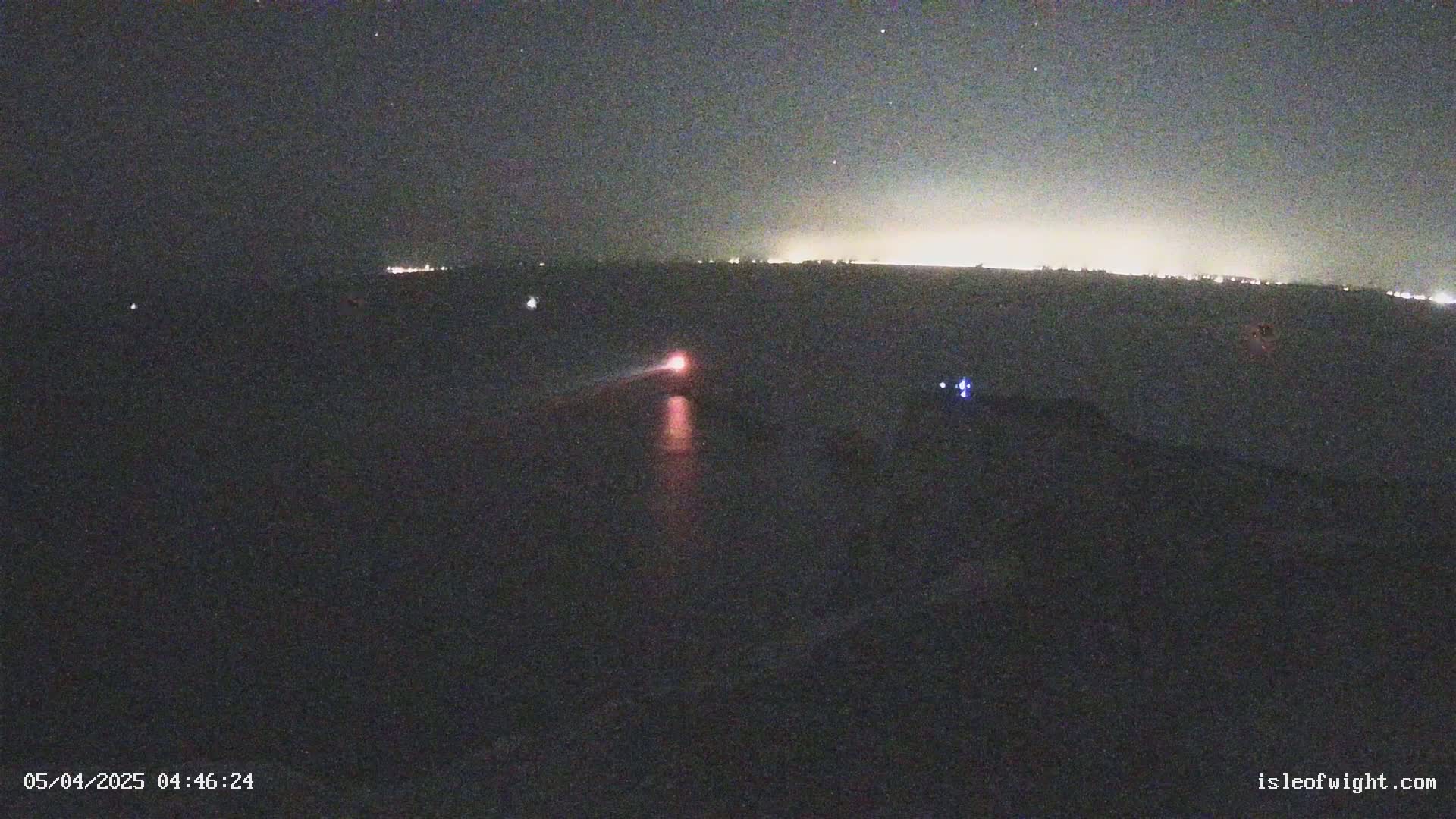 A nighttime long shot shows a distant, faintly lit horizon under a starry sky, with a single red light visible closer to the camera.