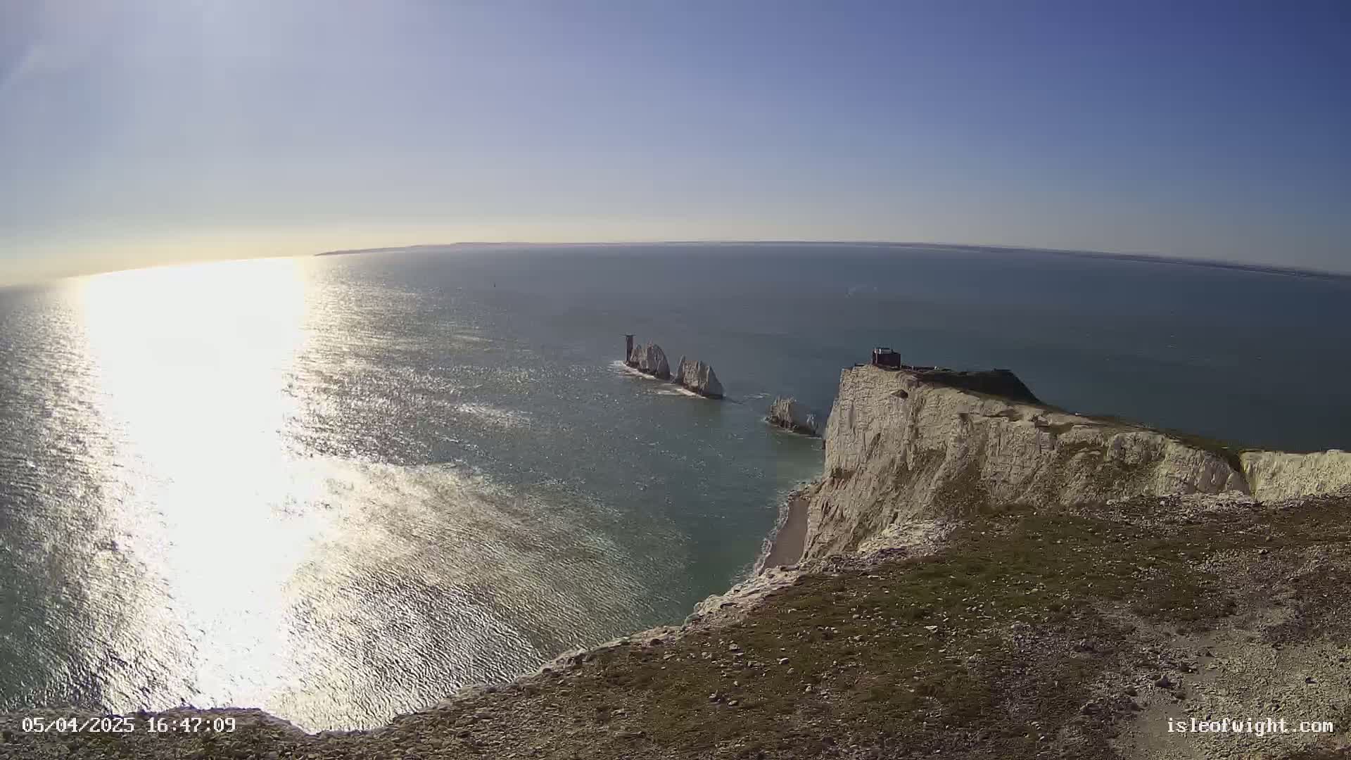 White cliffs overlook a body of water on a sunny day, with several smaller white rock formations visible in the distance.