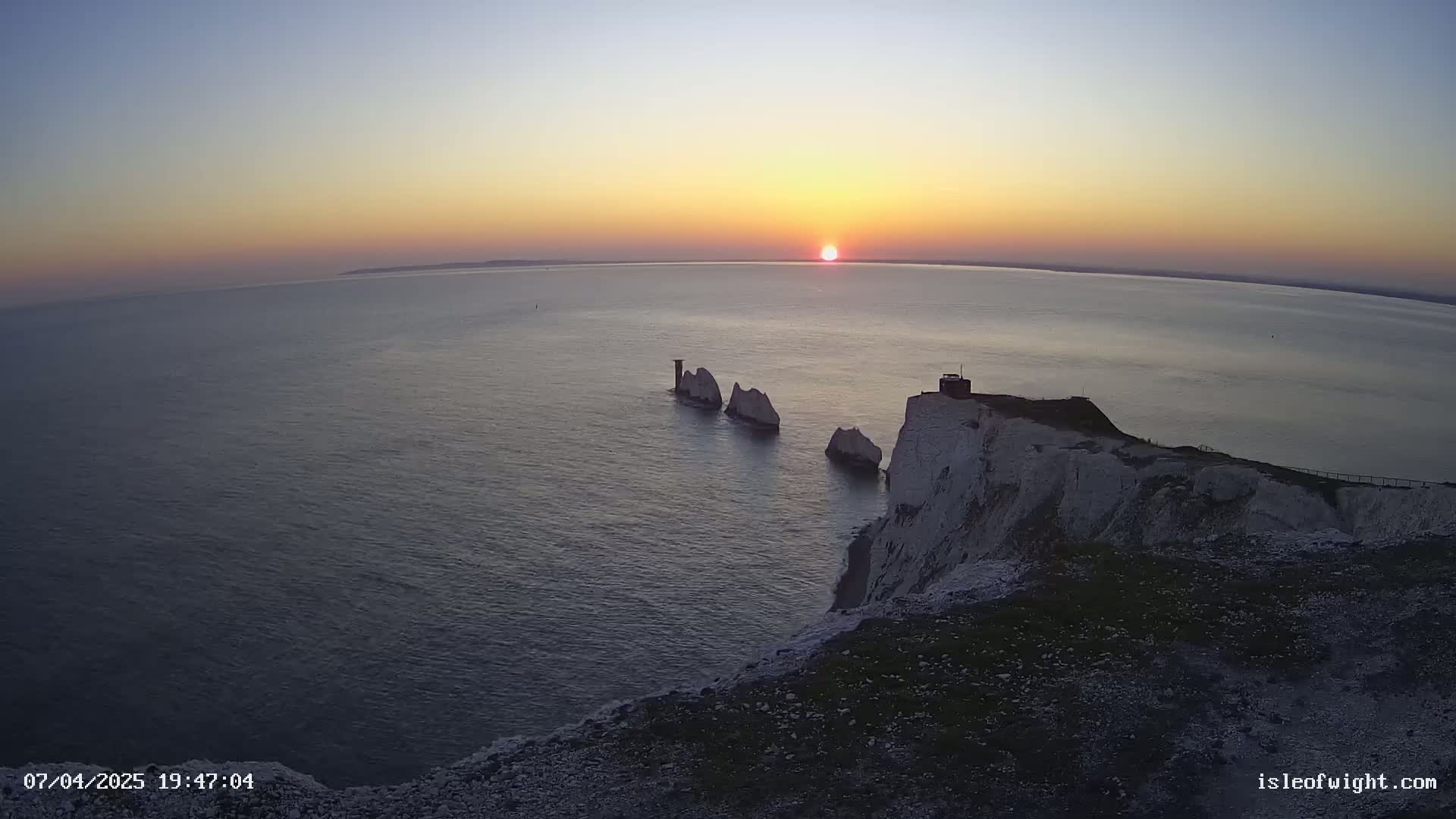 A sunset over a calm ocean, showcasing white cliffs and several stacks of rock formations in the water.