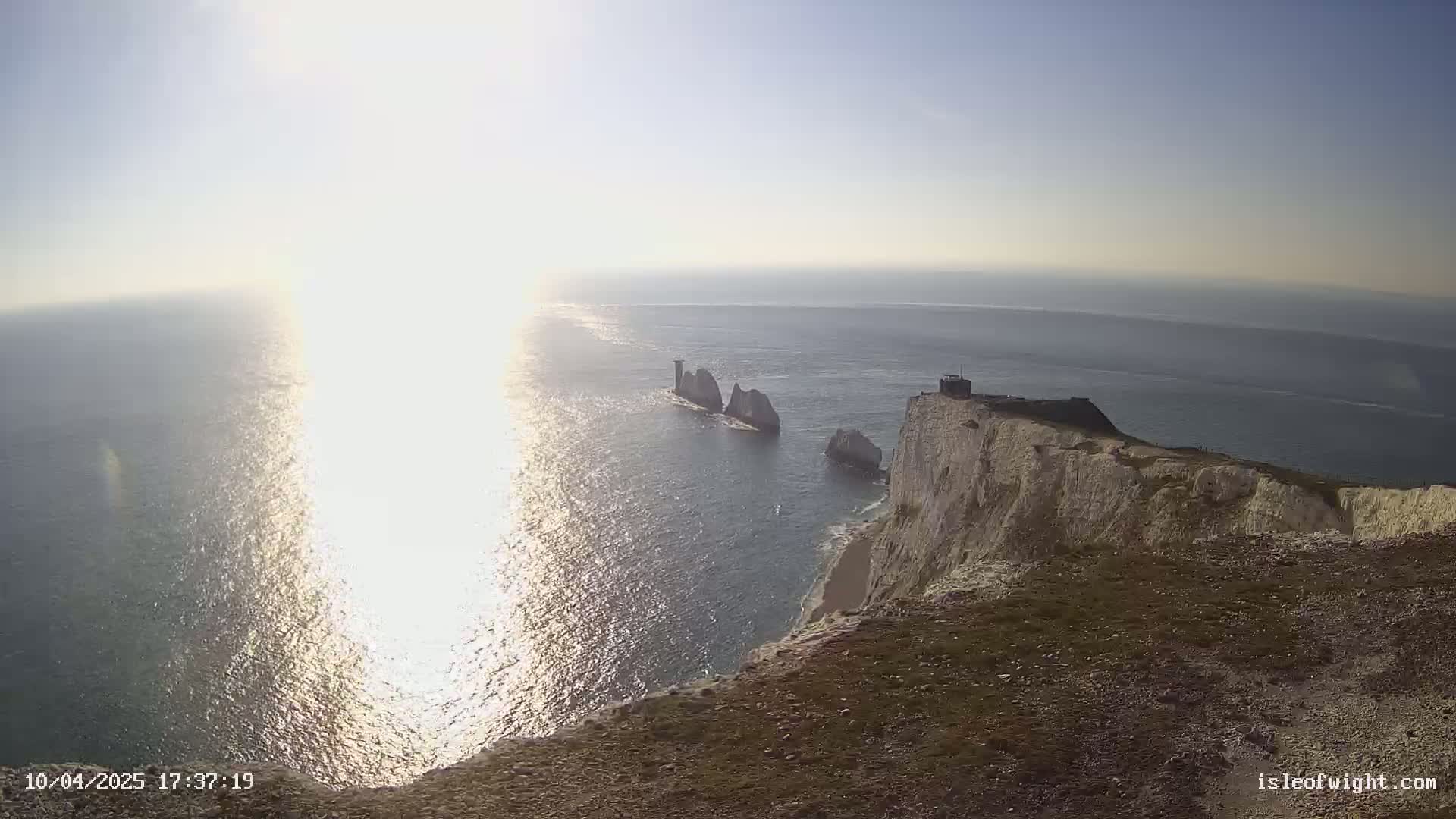 A bright, sunny day reveals a dramatic cliffside overlooking the ocean, with several prominent rock formations visible in the water below.