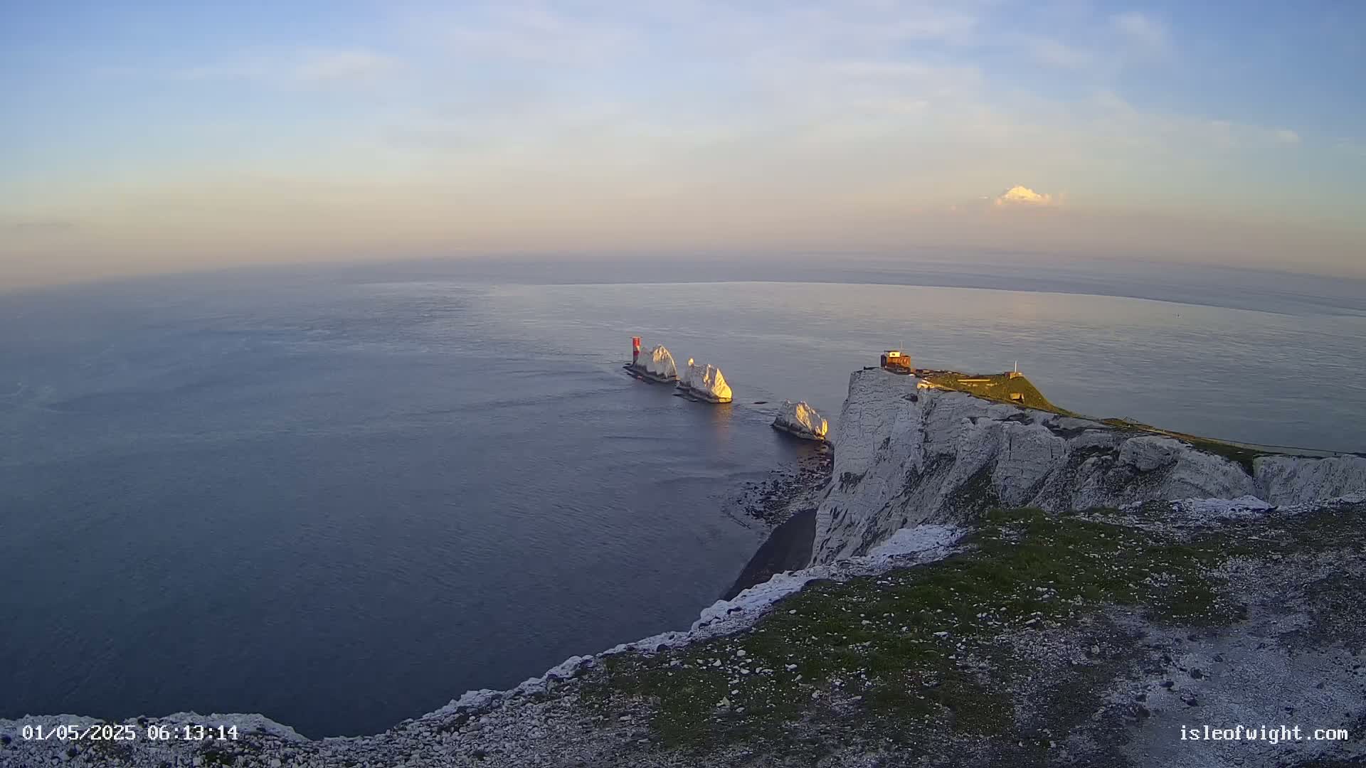 White cliffs overlook a calm sea at sunset, with several white rock formations visible in the water.