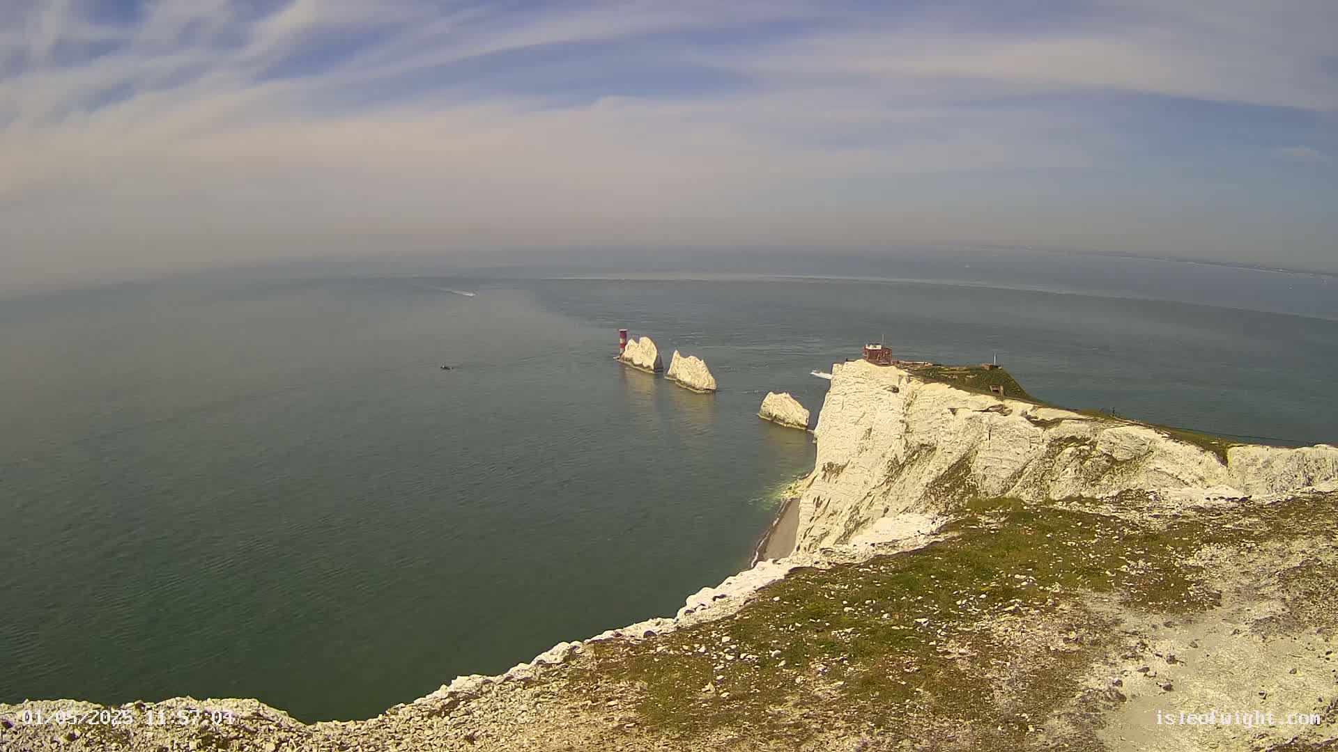 White cliffs overlook a calm, hazy sea with several stacks and a small building visible on the cliff edge.