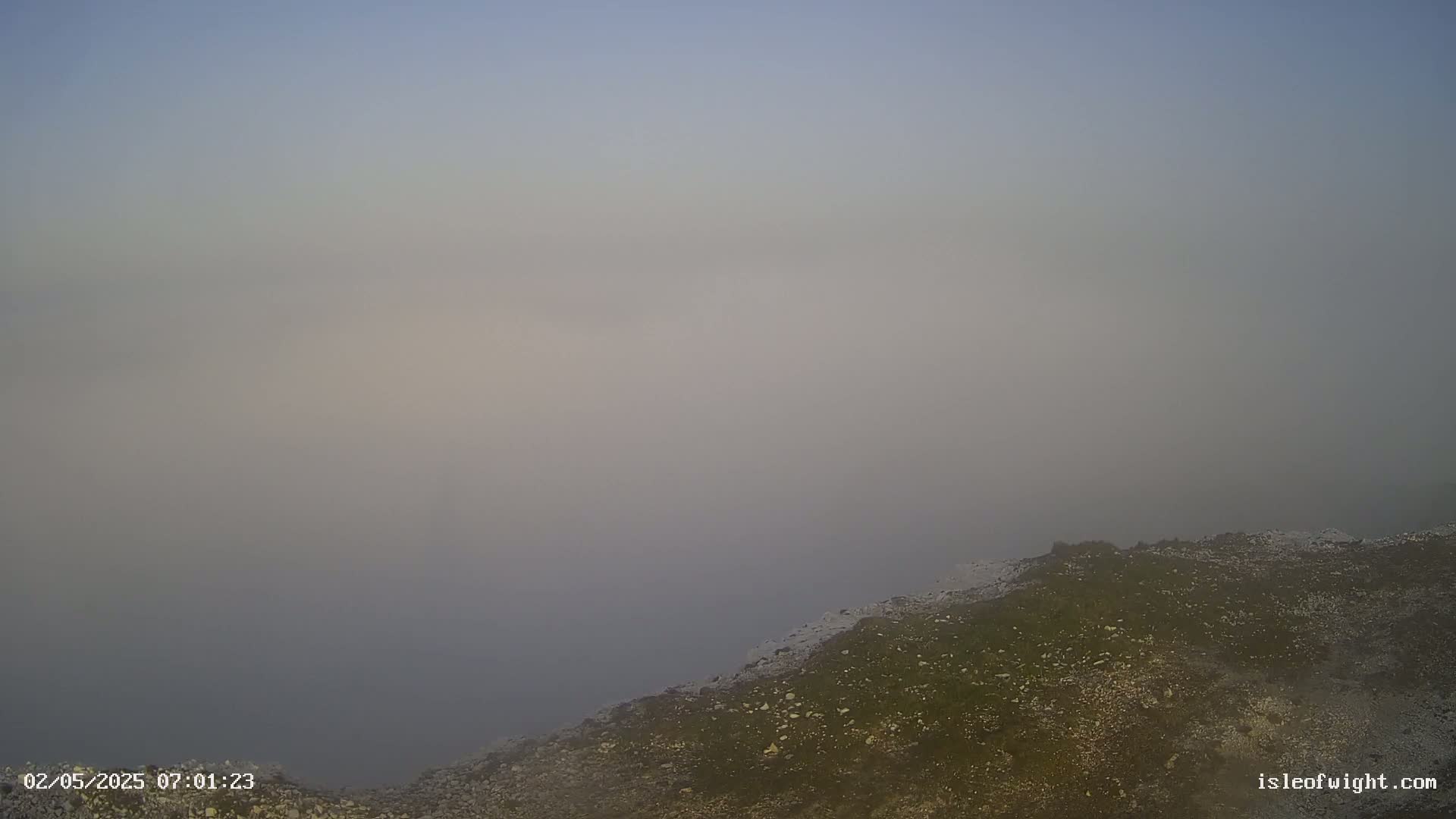 A foggy expanse of water meets a rocky, sparsely vegetated shoreline.