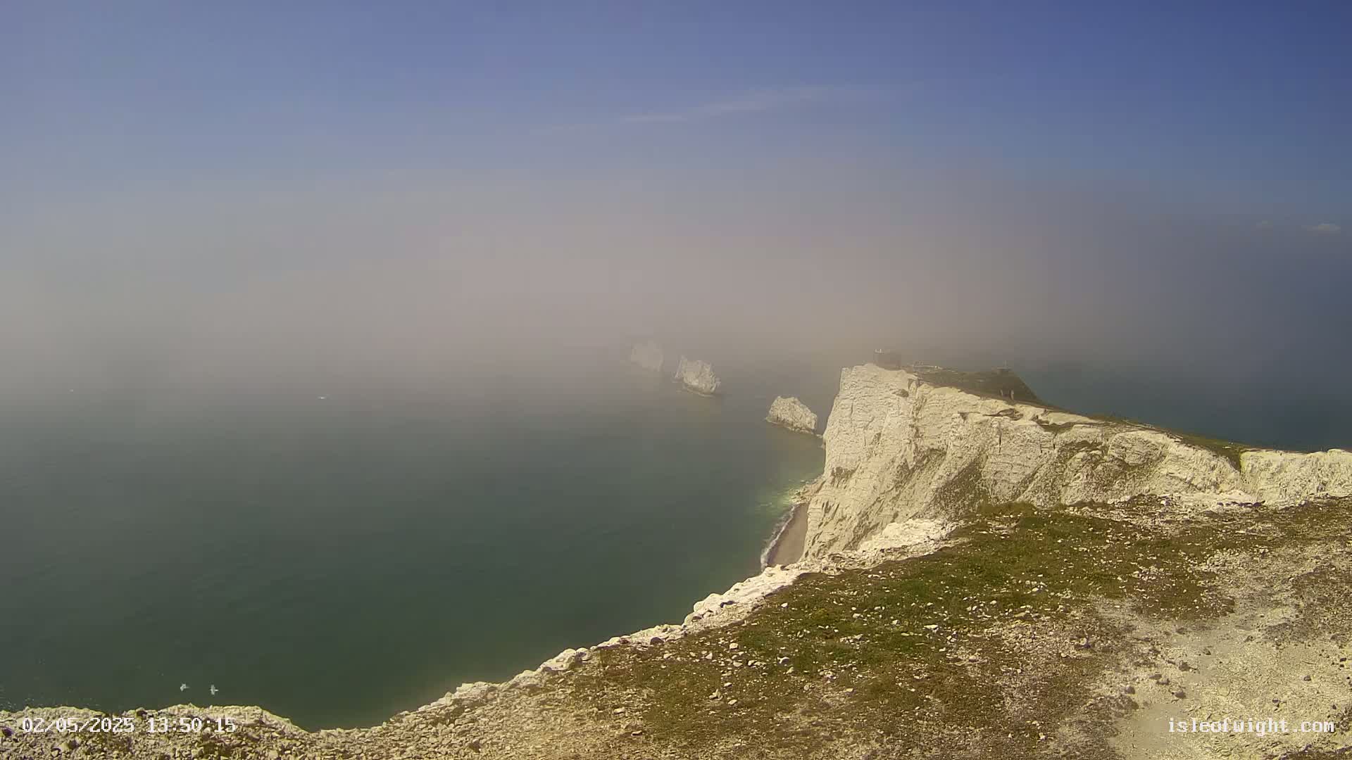 White cliffs overlooking a hazy sea with several smaller rock formations visible in the distance.