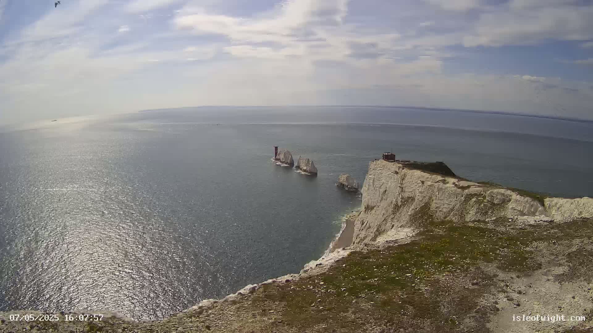 A view from a clifftop shows white chalk cliffs and stacks in a calm, sunny sea.