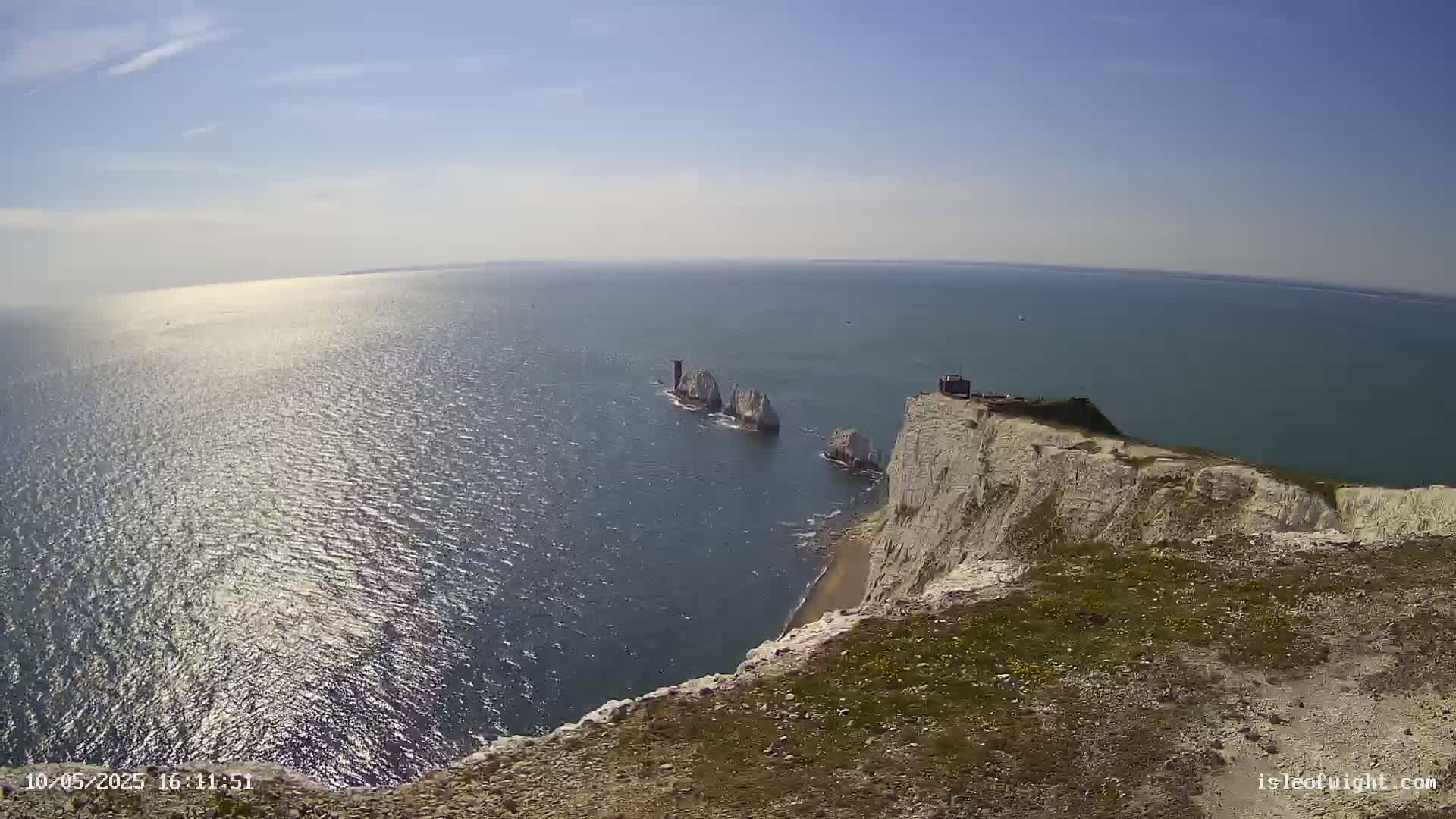 White cliffs overlook a calm, sunlit sea where several small, rocky islands are visible in the distance.