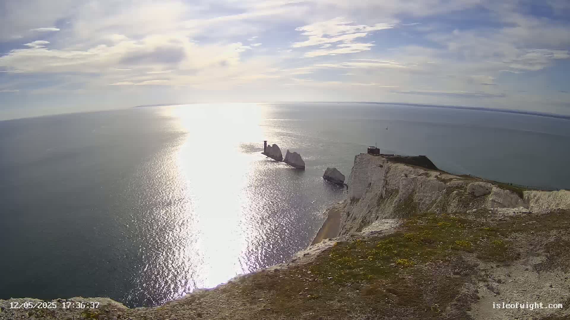 A sunny day shows white cliffs overlooking a sparkling sea with several distant rock formations.