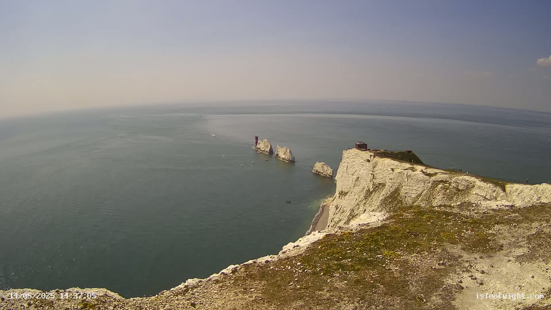 White cliffs overlook a calm sea with several small rocky islands in the distance under a hazy sky.